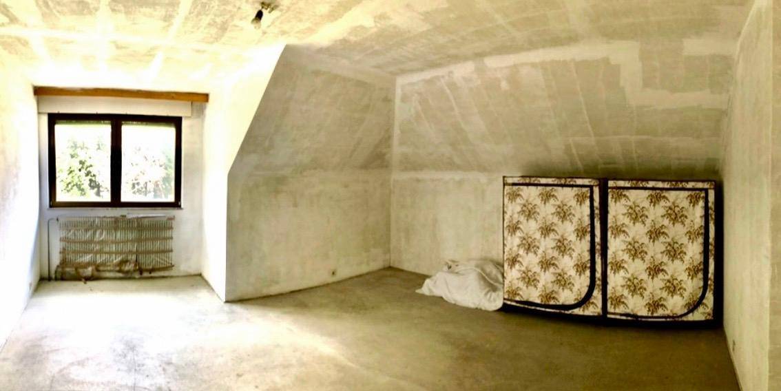 Dachgeschossraum mit schrägen Wänden, Fenster und einem Stoffschrank.