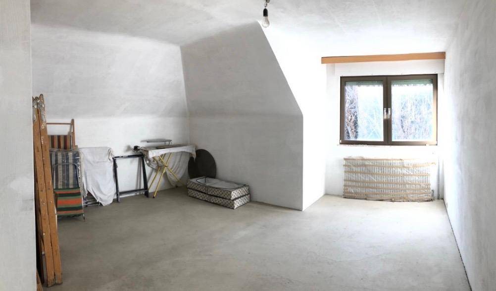 Leerer Dachgeschossraum mit schrägen Wänden und Fenster, bereit für Ausbau.