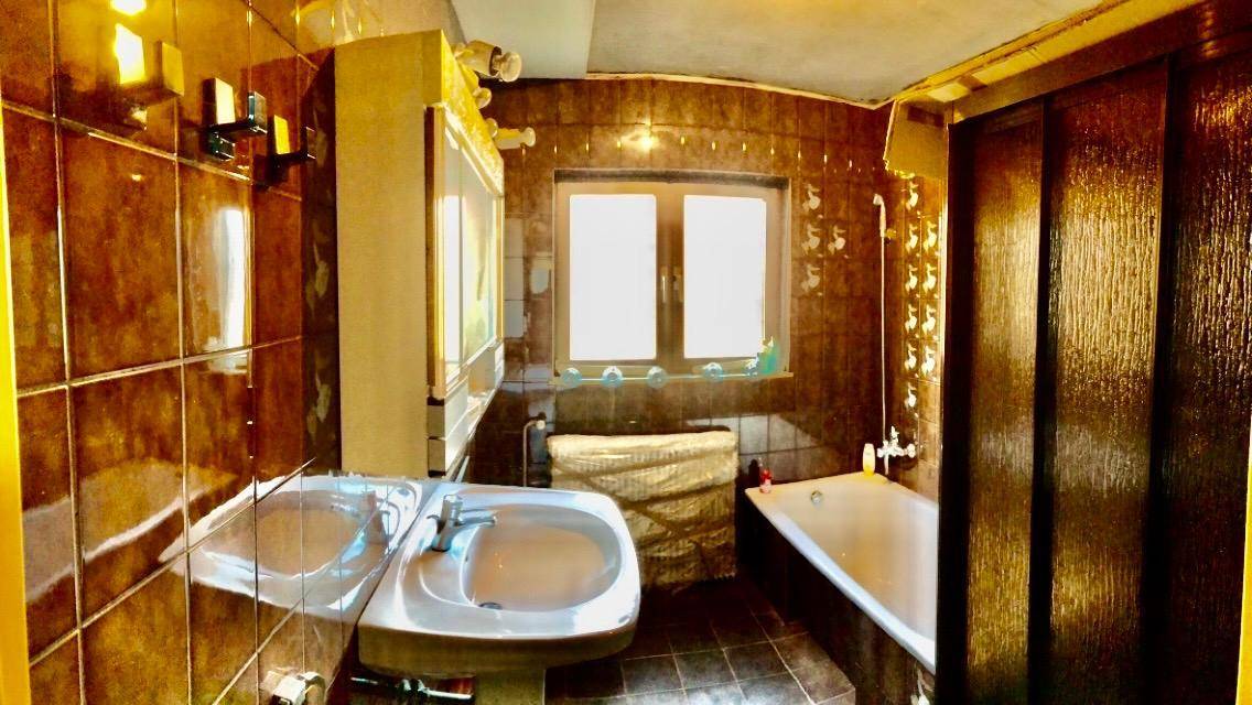 Badezimmer mit braunen Fliesen, Badewanne, Doppelwaschbecken und Fenster.