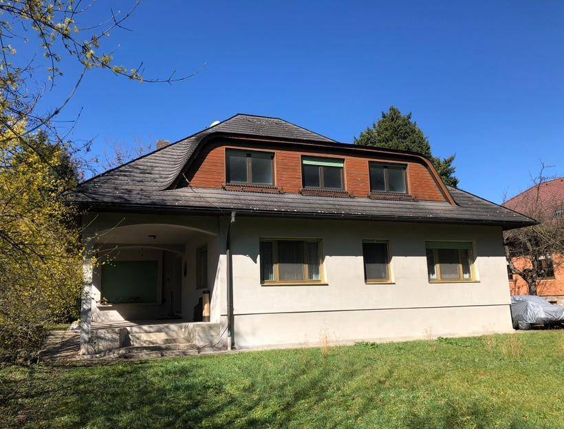 Freistehendes Einfamilienhaus mit großem Garten und Mansarddach an einem sonnigen Tag.