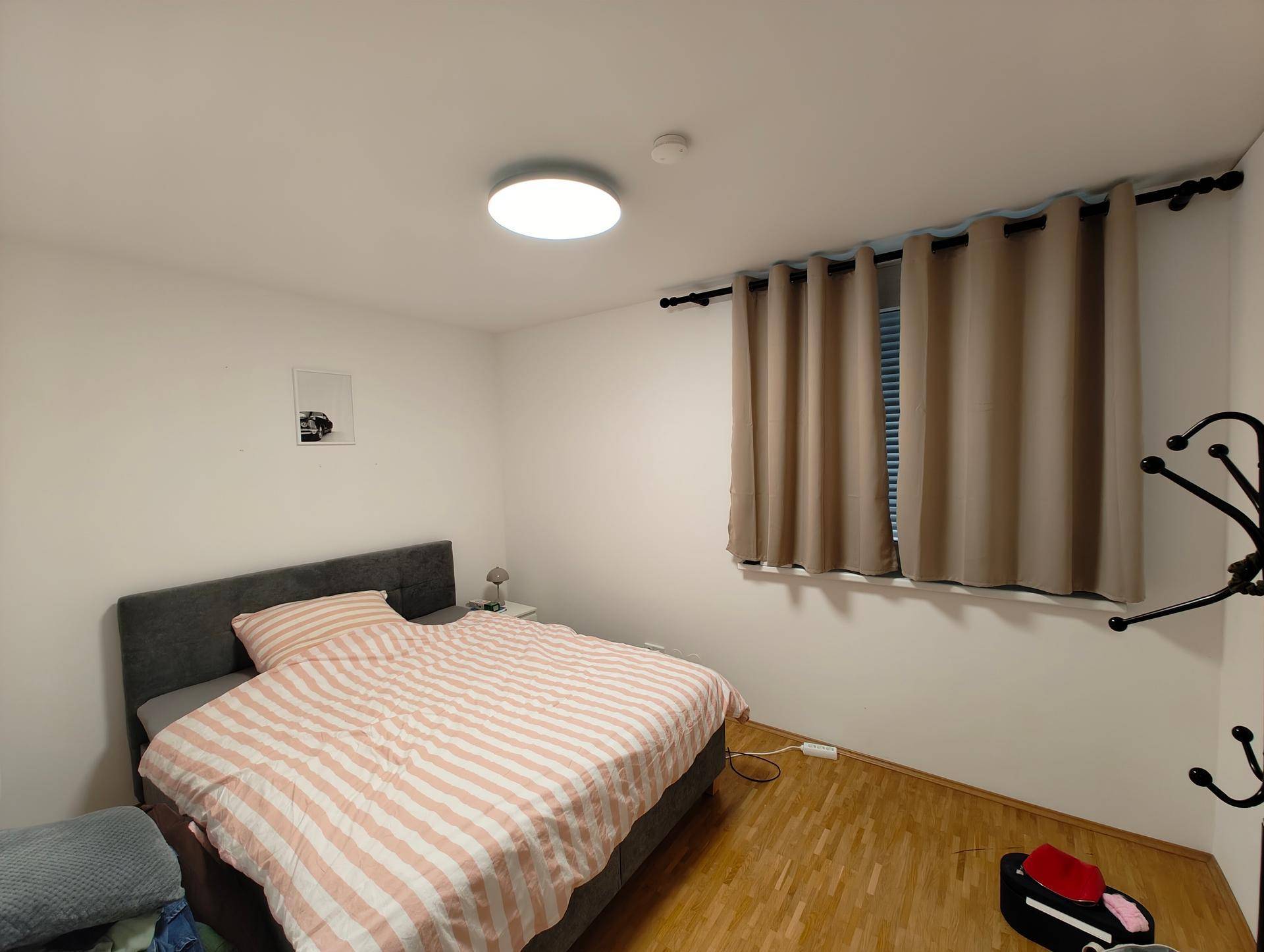 Gemütliches Schlafzimmer mit Doppelbett, Holzboden und blickdichten Vorhängen am Fenster.
