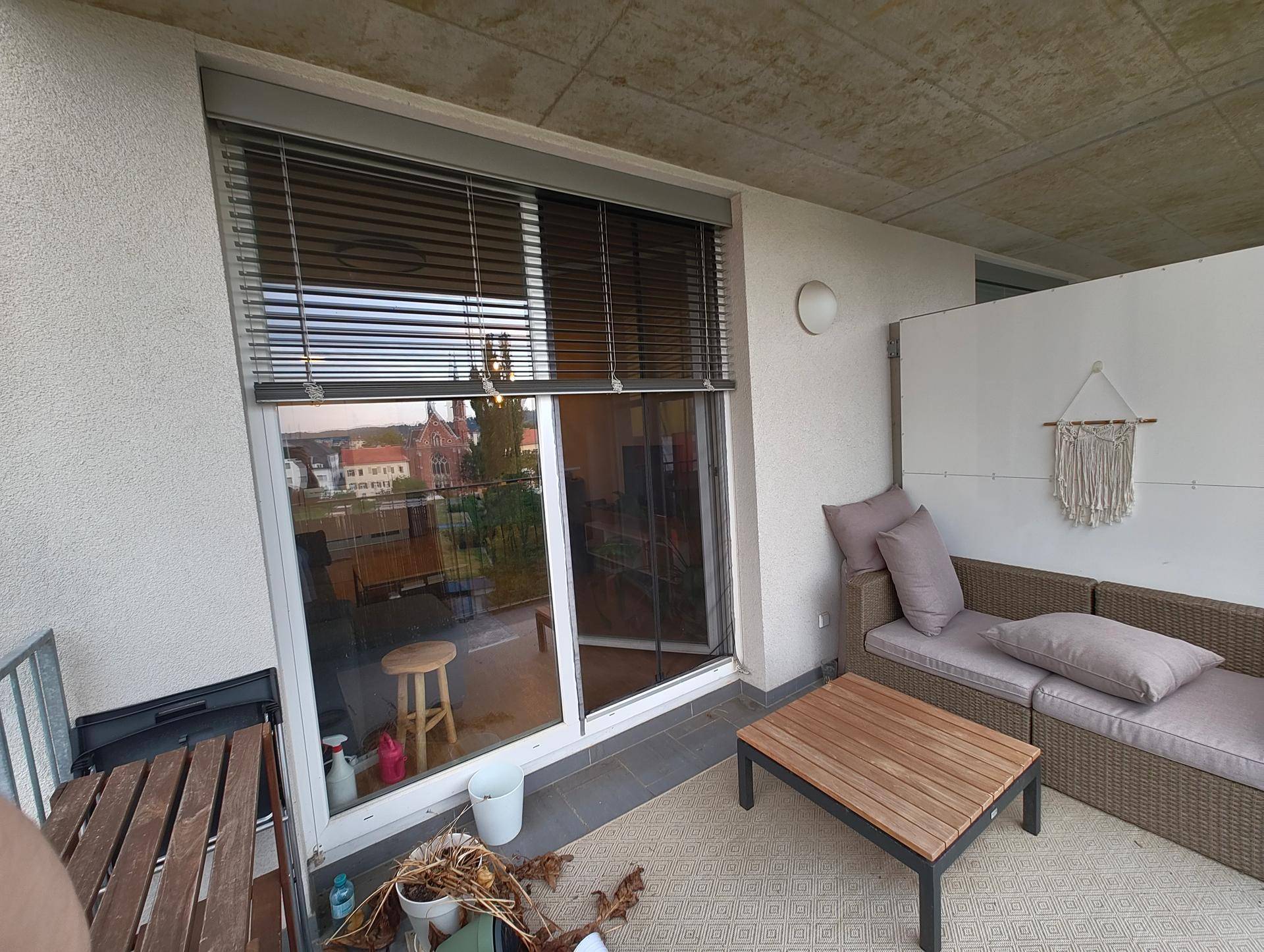 Balkon mit modernen Outdoor-Möbeln und Blick auf die Umgebung durch die Jalousien.