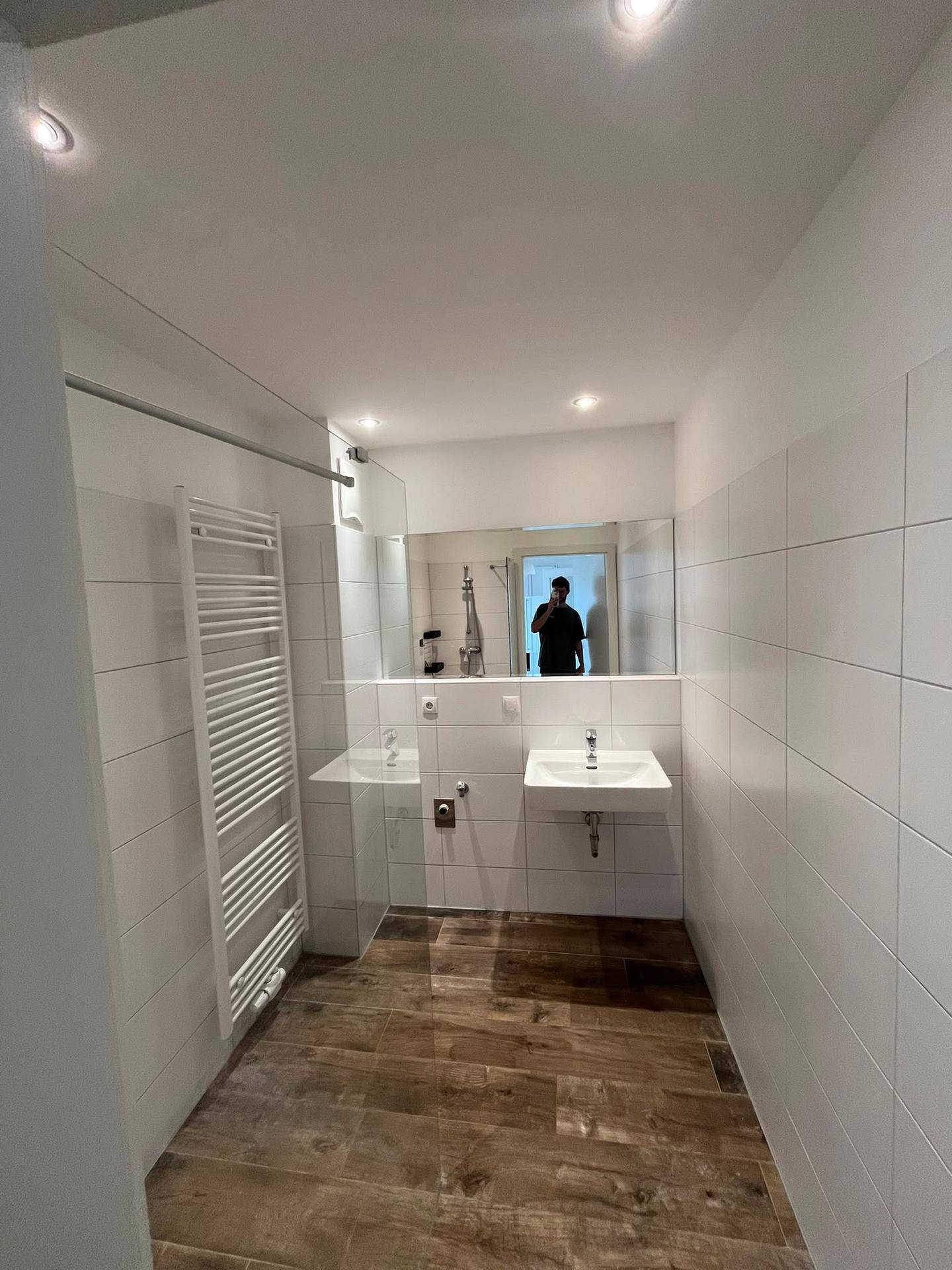 Helles Badezimmer mit Einzelwaschbecken, großem Spiegel und modernen Fliesen in Holzoptik.