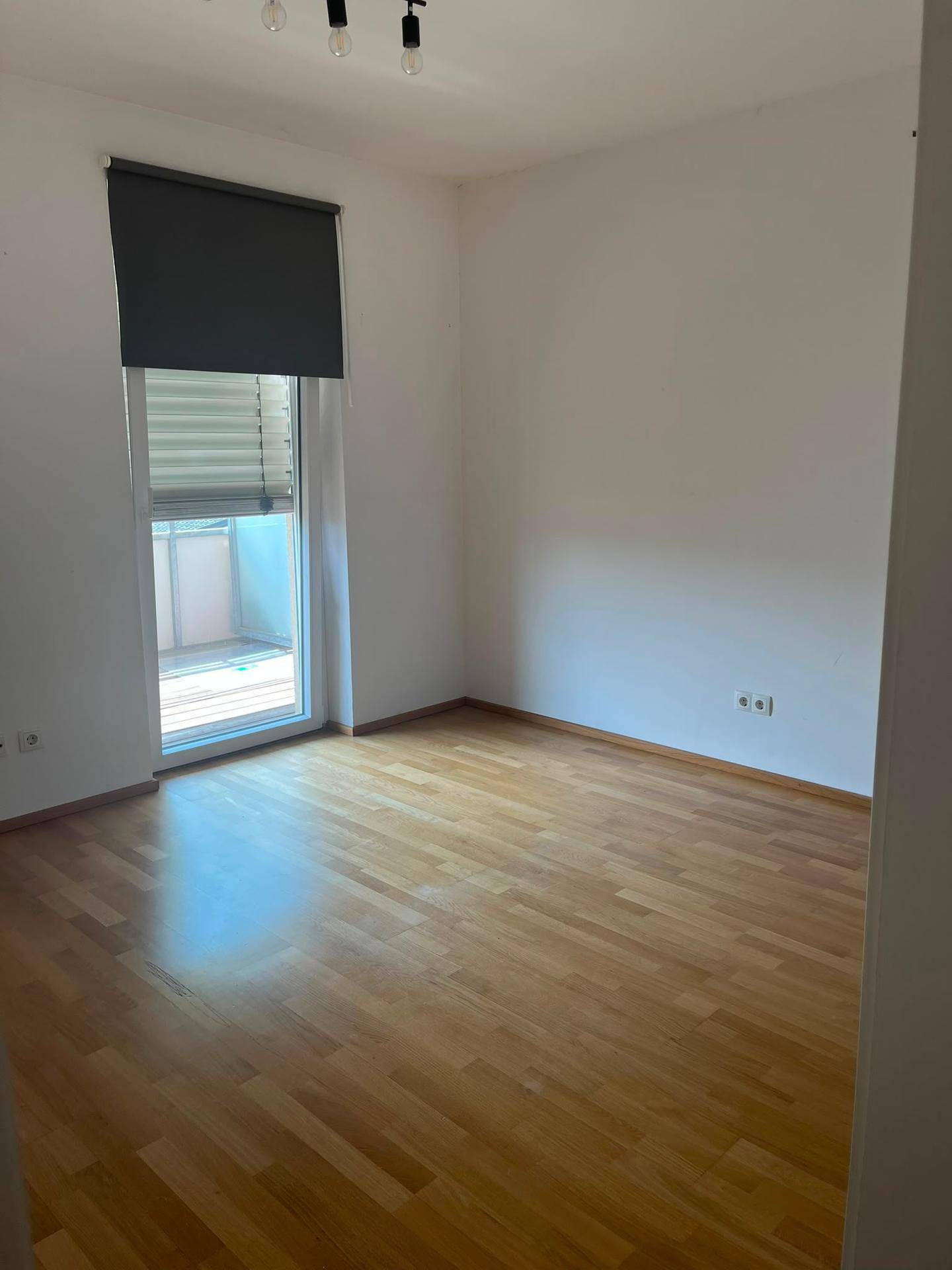 Helles Schlafzimmer mit Holzboden und Zugang zu einem Balkon, ausgestattet mit einem Rollladen.