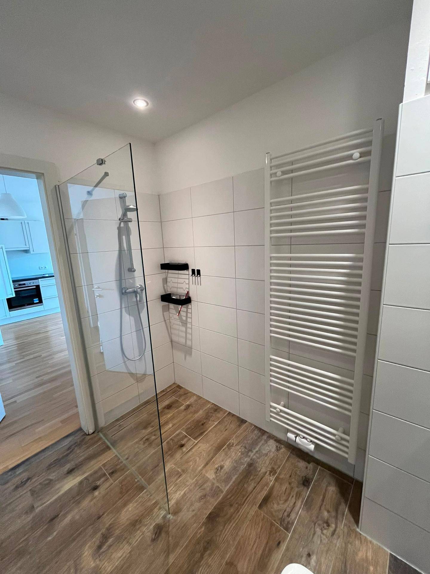 Modernes Badezimmer mit ebenerdiger Dusche, weißen Fliesen und einem beheizten Handtuchhalter.
