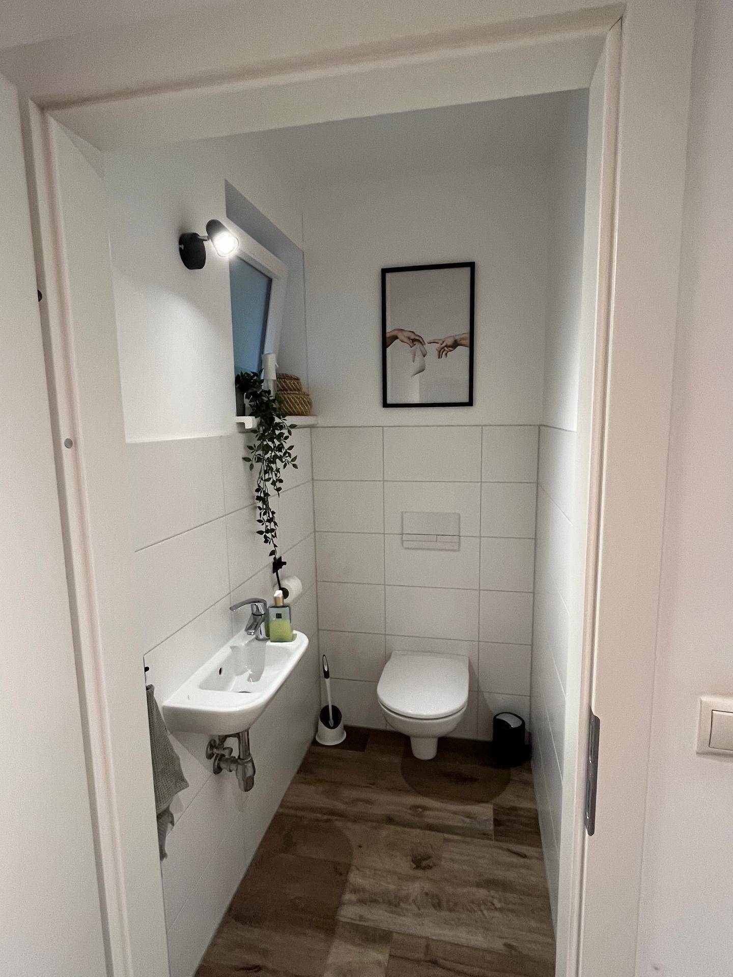 Modernes Gäste-WC mit Fenster, wandhängender Toilette und dekorativen Elementen.