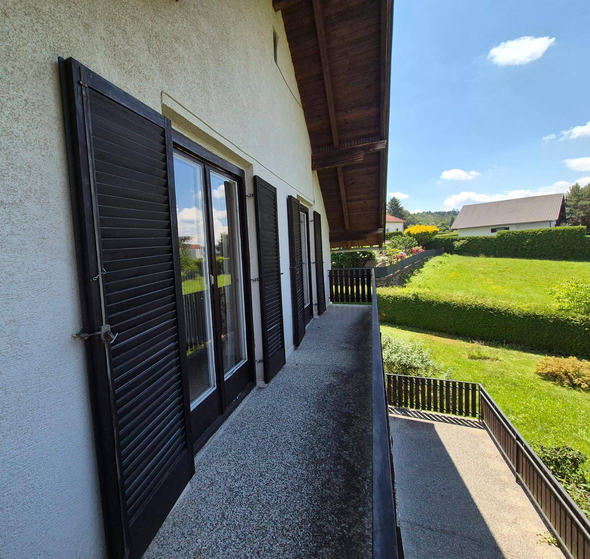 Balkon mit geschlossenen Fensterläden und Blick auf die grüne, hügelige Umgebung.