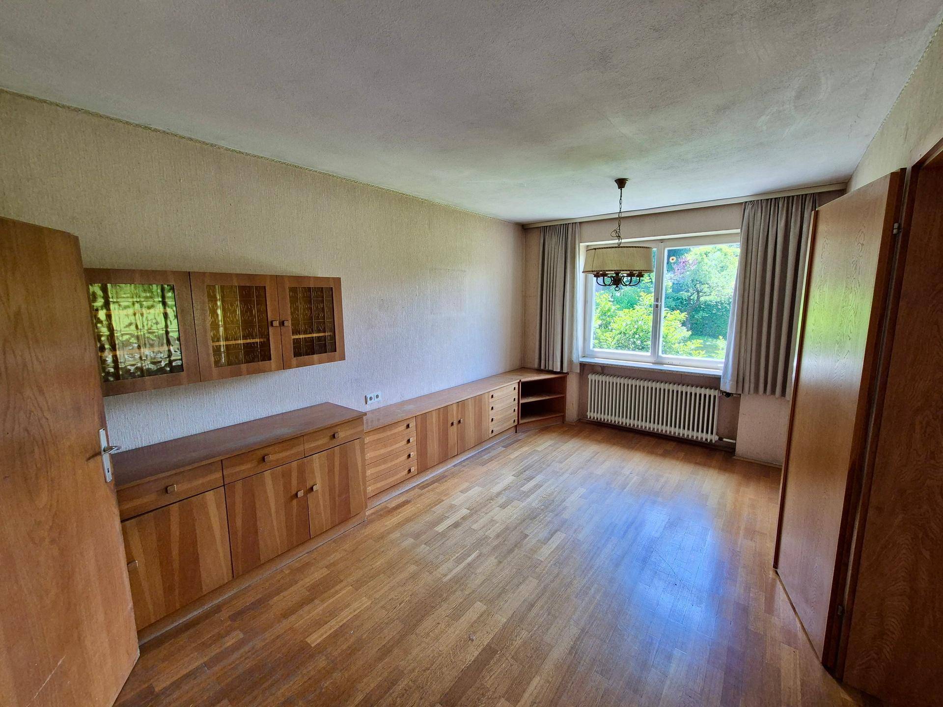 Helles Zimmer mit Parkettboden, einem Fenster und niedrigen Holzschränken entlang der Wand.
