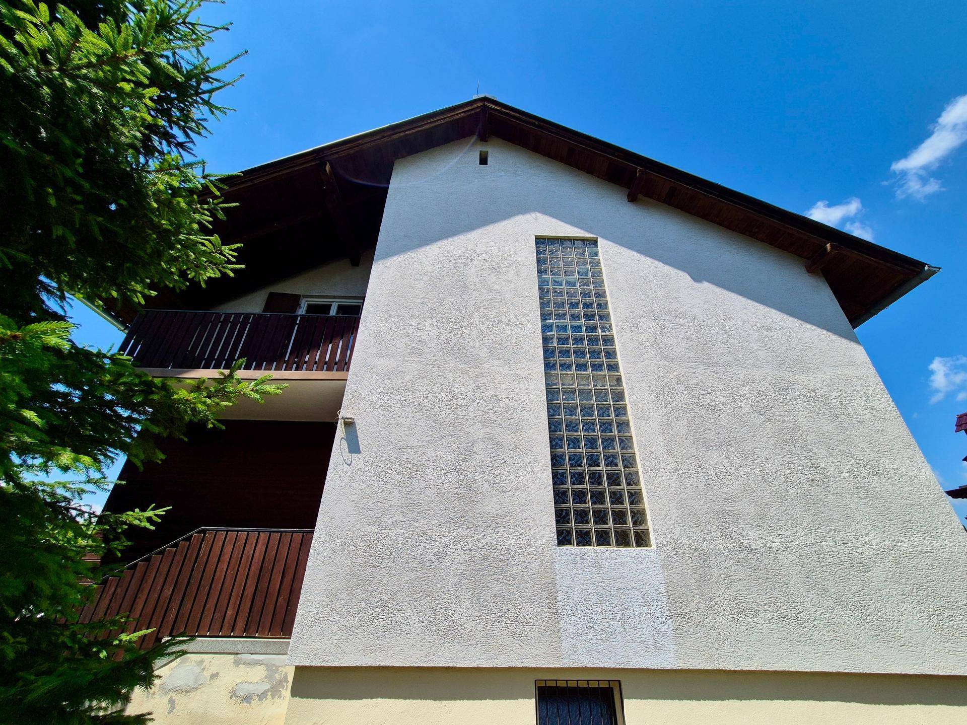 Seitenansicht des Hauses mit vertikalem Glasbausteinfenster und einem Holzbalkon.