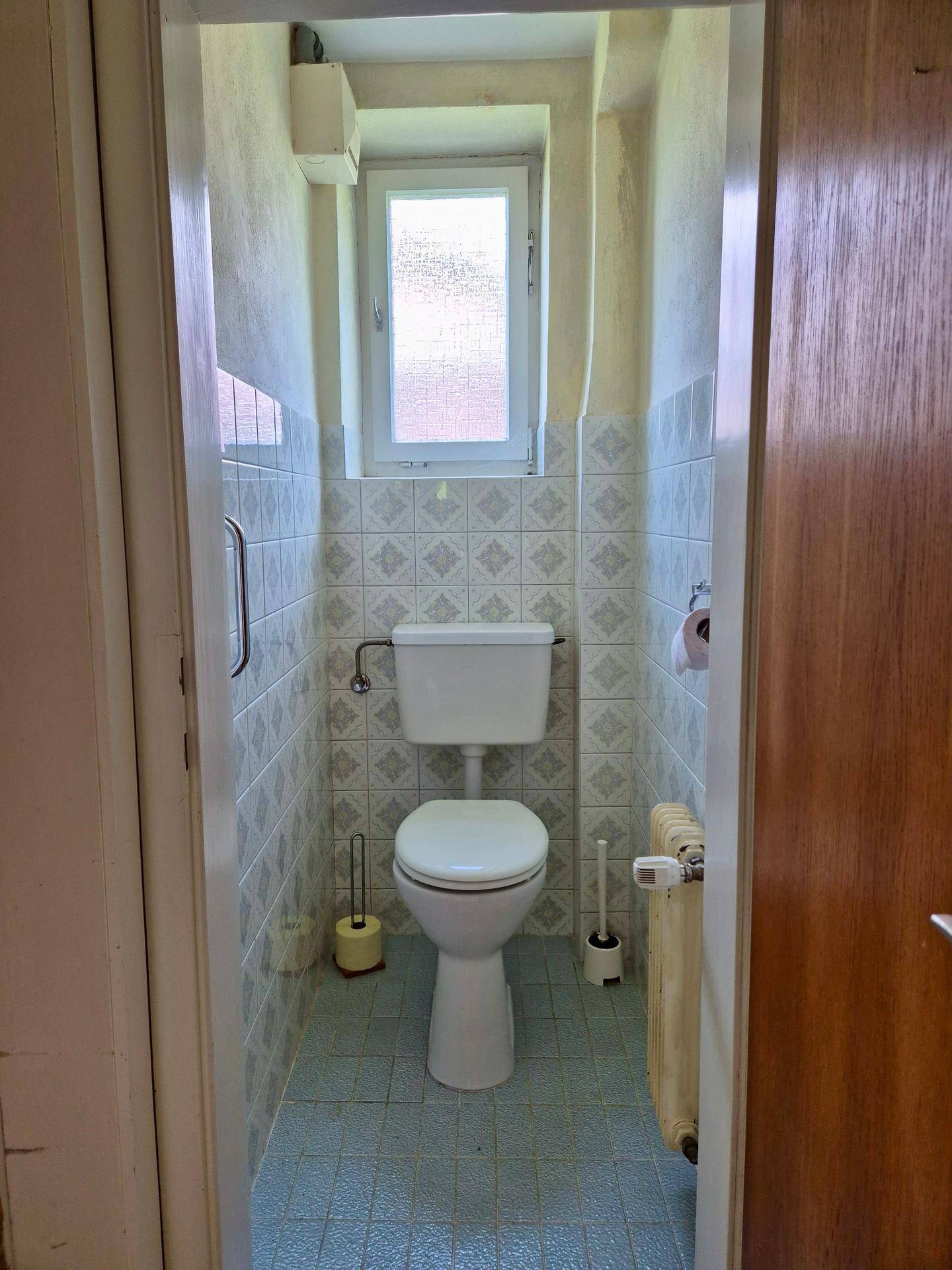 Kleines Gäste-WC mit gemusterten Fliesen, Fenster und Heizkörper.