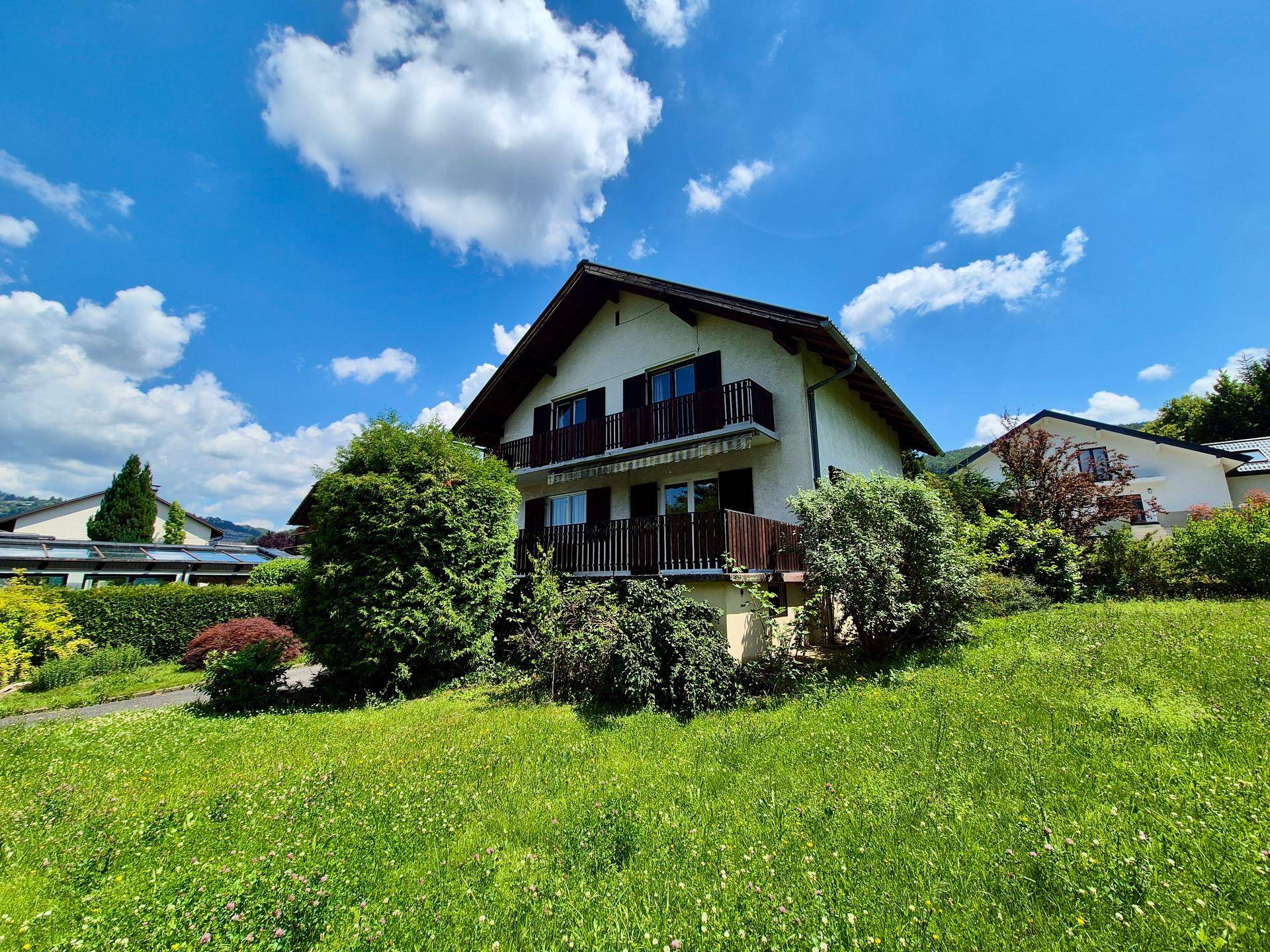 Freistehendes Haus mit mehreren Balkonen, umgeben von einer weitläufigen grünen Wiese und Bäumen.