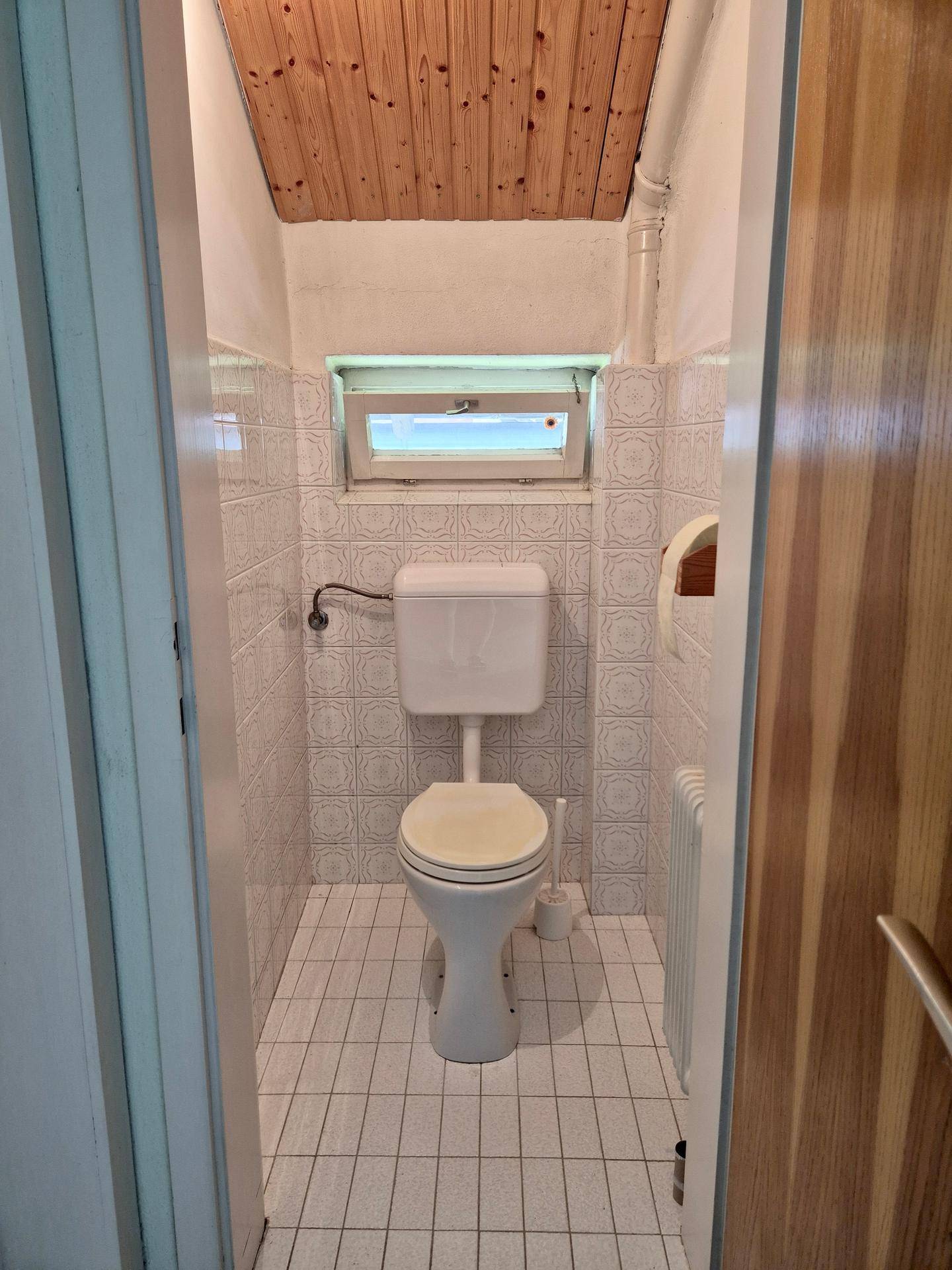 Einfaches Gäste-WC mit weißen Fliesen, Fenster und Heizkörper.