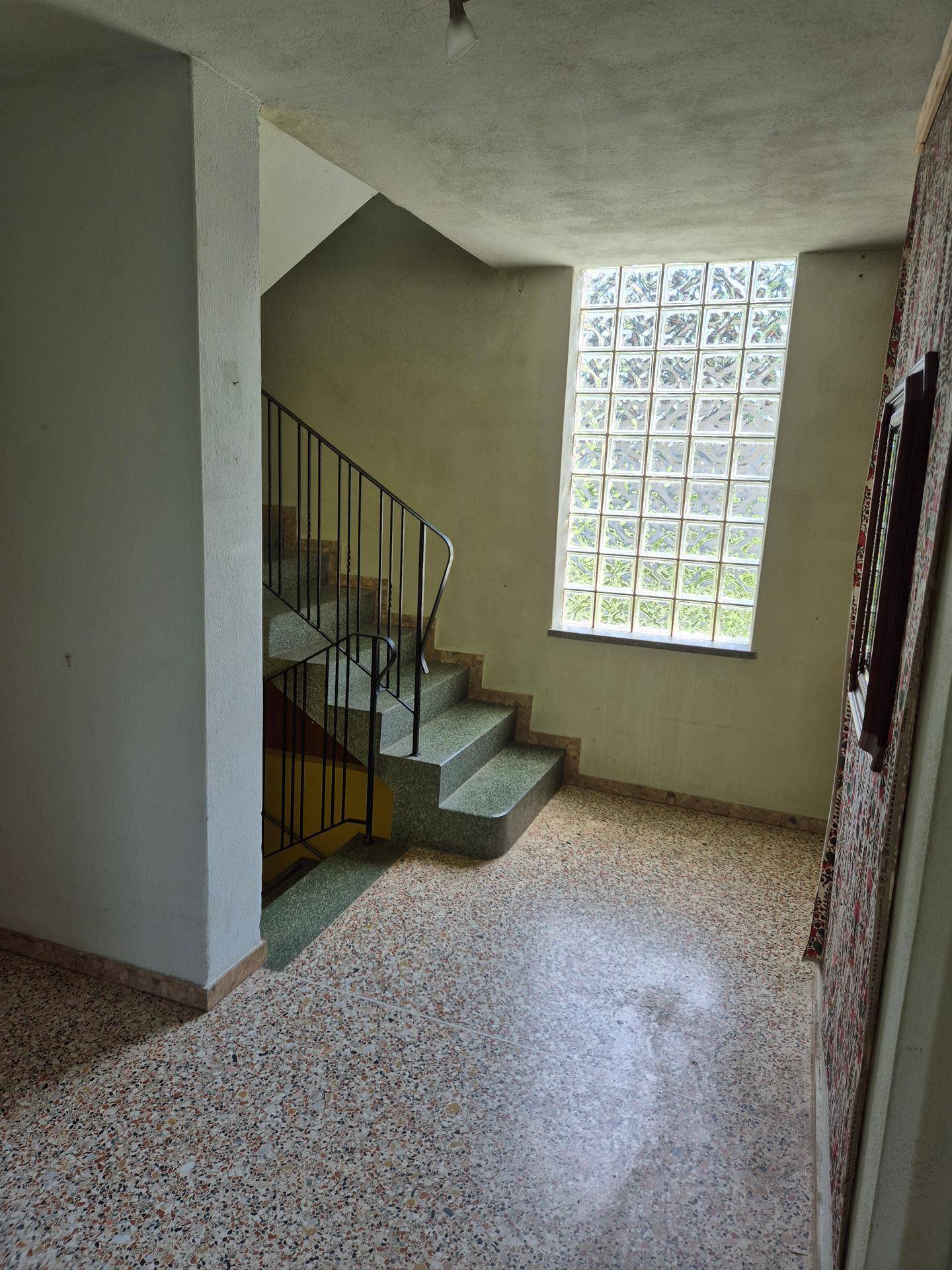 Heller Flur mit Terrazzoboden und Treppe, beleuchtet durch ein großes Glasbausteinfenster.