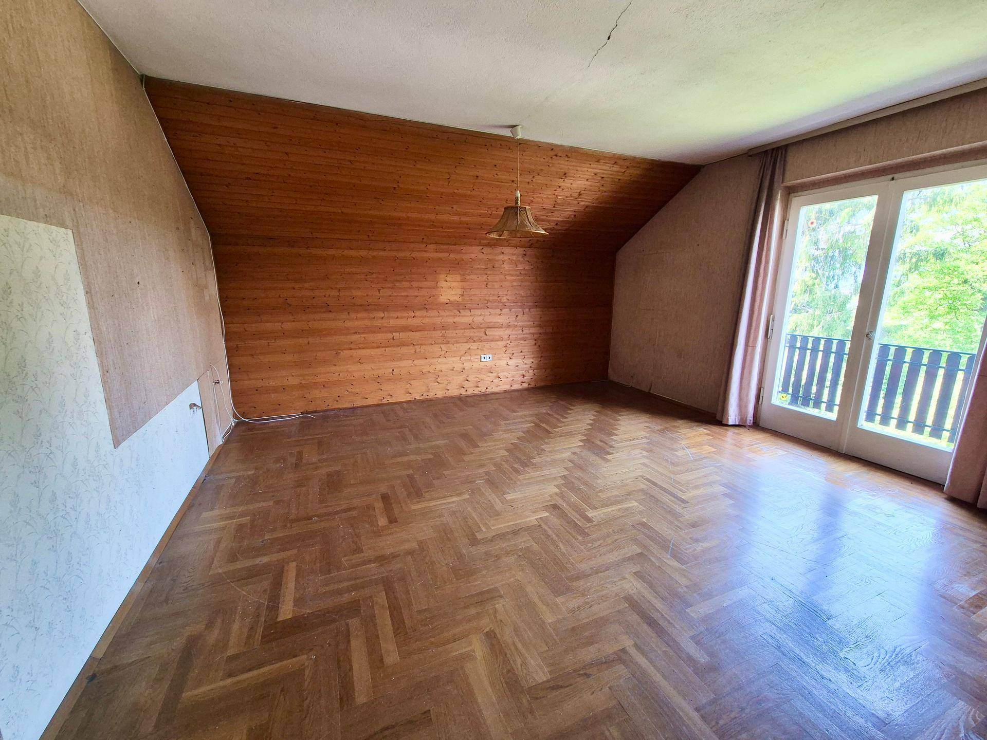 Helles Schlafzimmer mit Parkettboden, Holzvertäfelung und Balkonzugang unter Dachschräge.