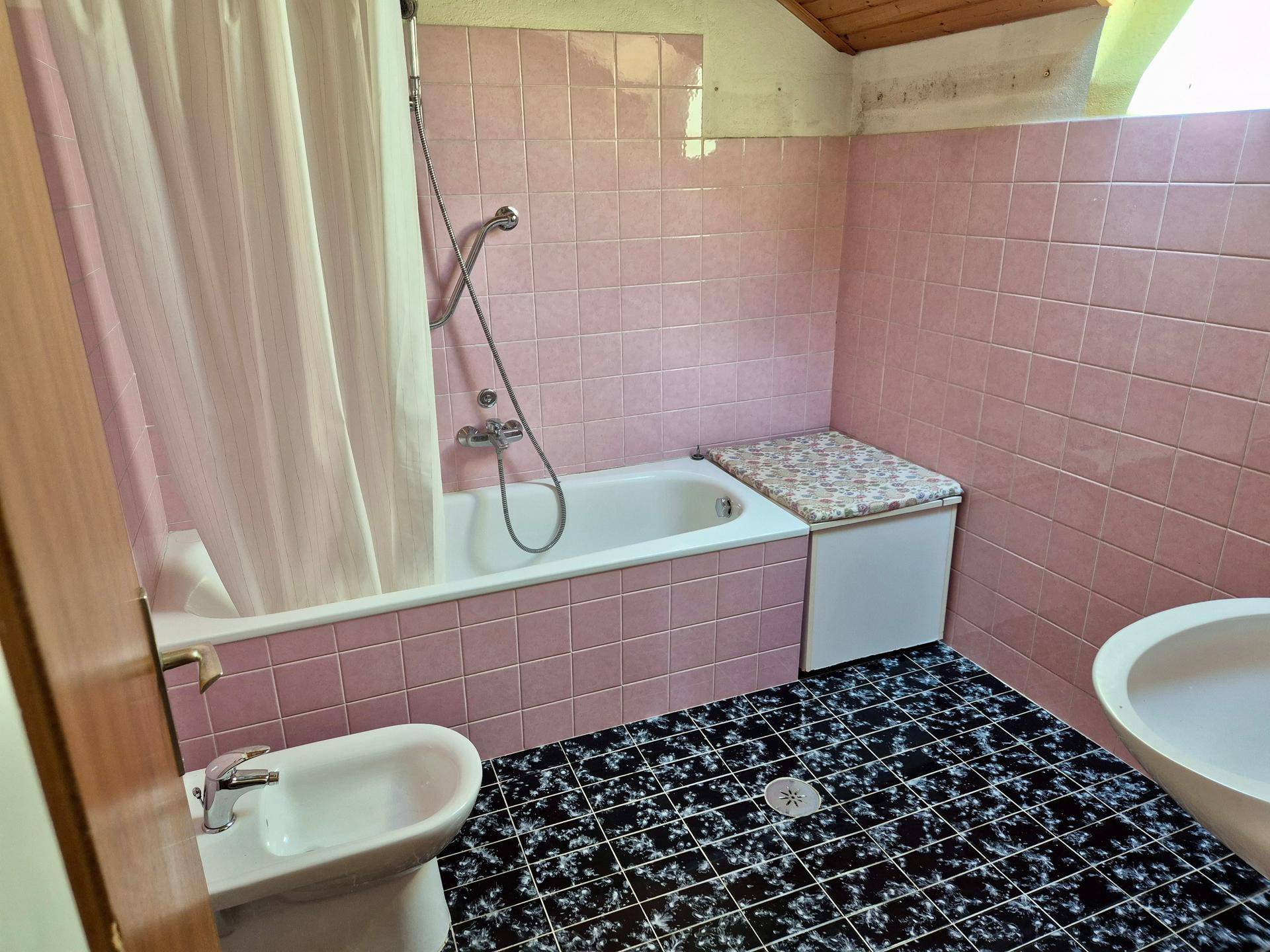 Badezimmer mit rosa Fliesen, Badewanne mit Duschvorhang und Bidet.
