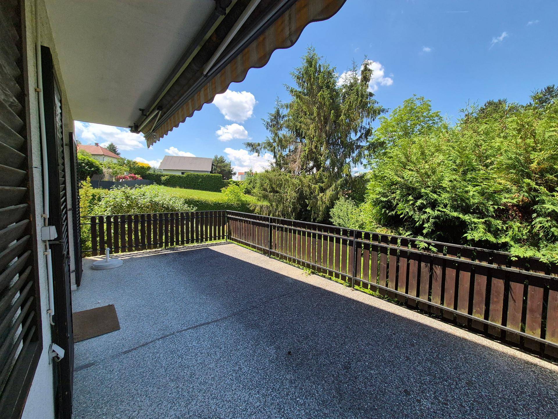 Großer Balkon mit Markise und weitem Blick über grüne Hügel und benachbarte Häuser.