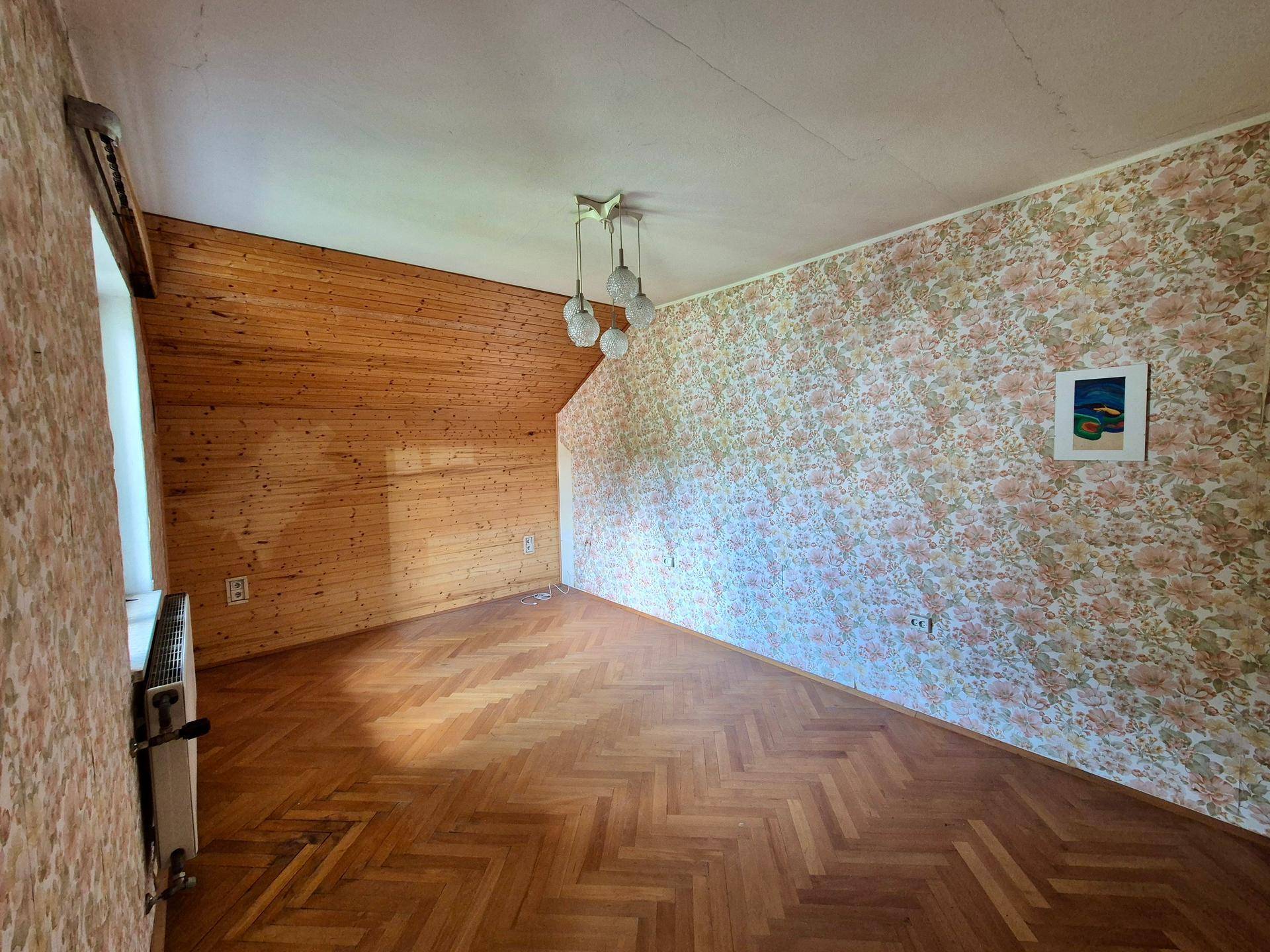 Gemütliches Schlafzimmer mit Parkettboden, Holzvertäfelung und floraler Tapete unter Dachschräge.