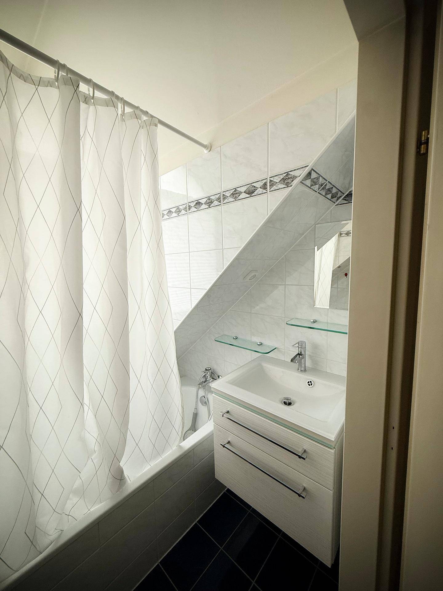 Badezimmer mit Badewanne, Duschvorhang und Waschbecken unter einer Dachschräge.