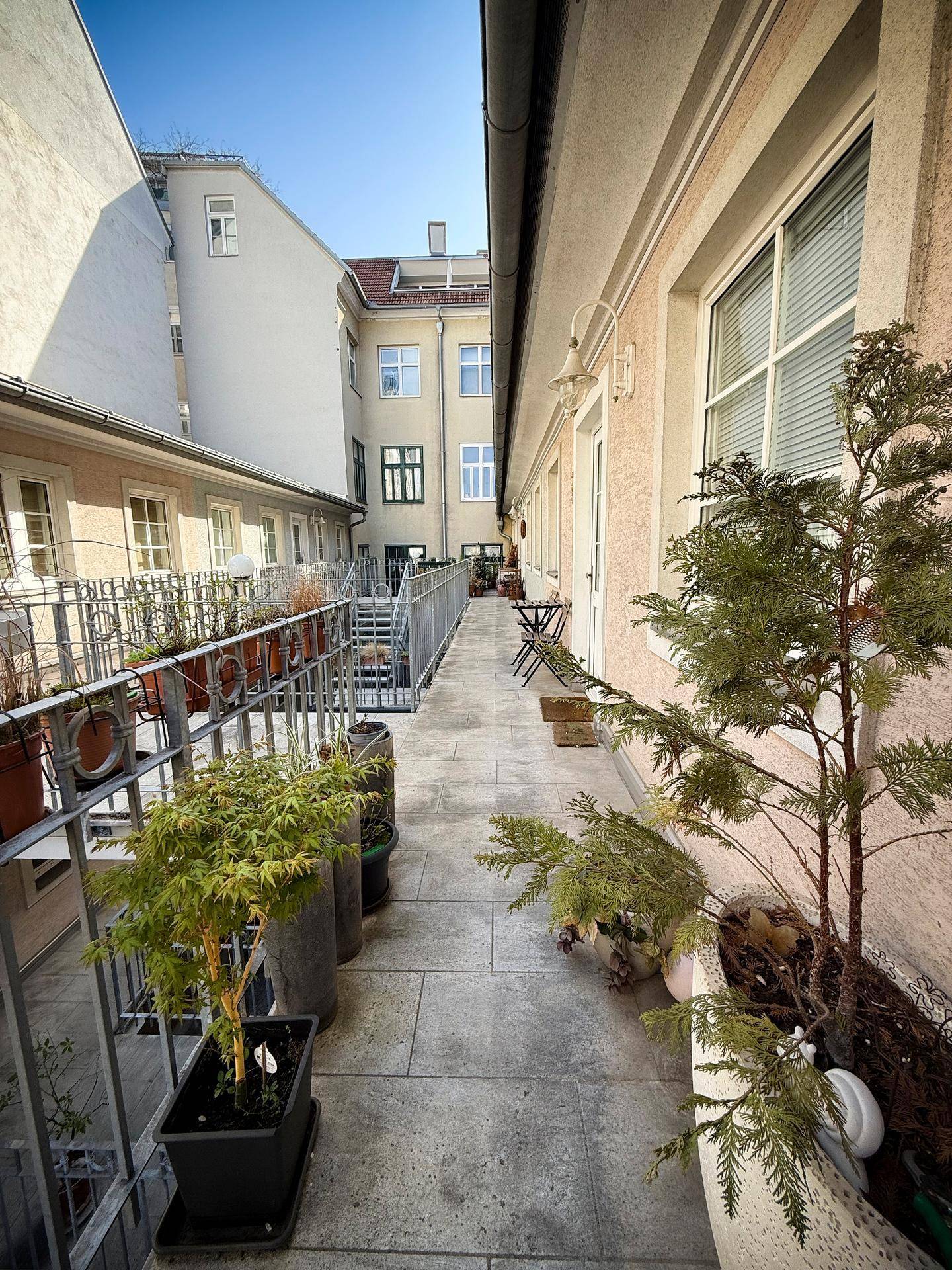 Langer, schmaler Balkon mit vielen Topfpflanzen und Blick auf die umliegenden Gebäude.