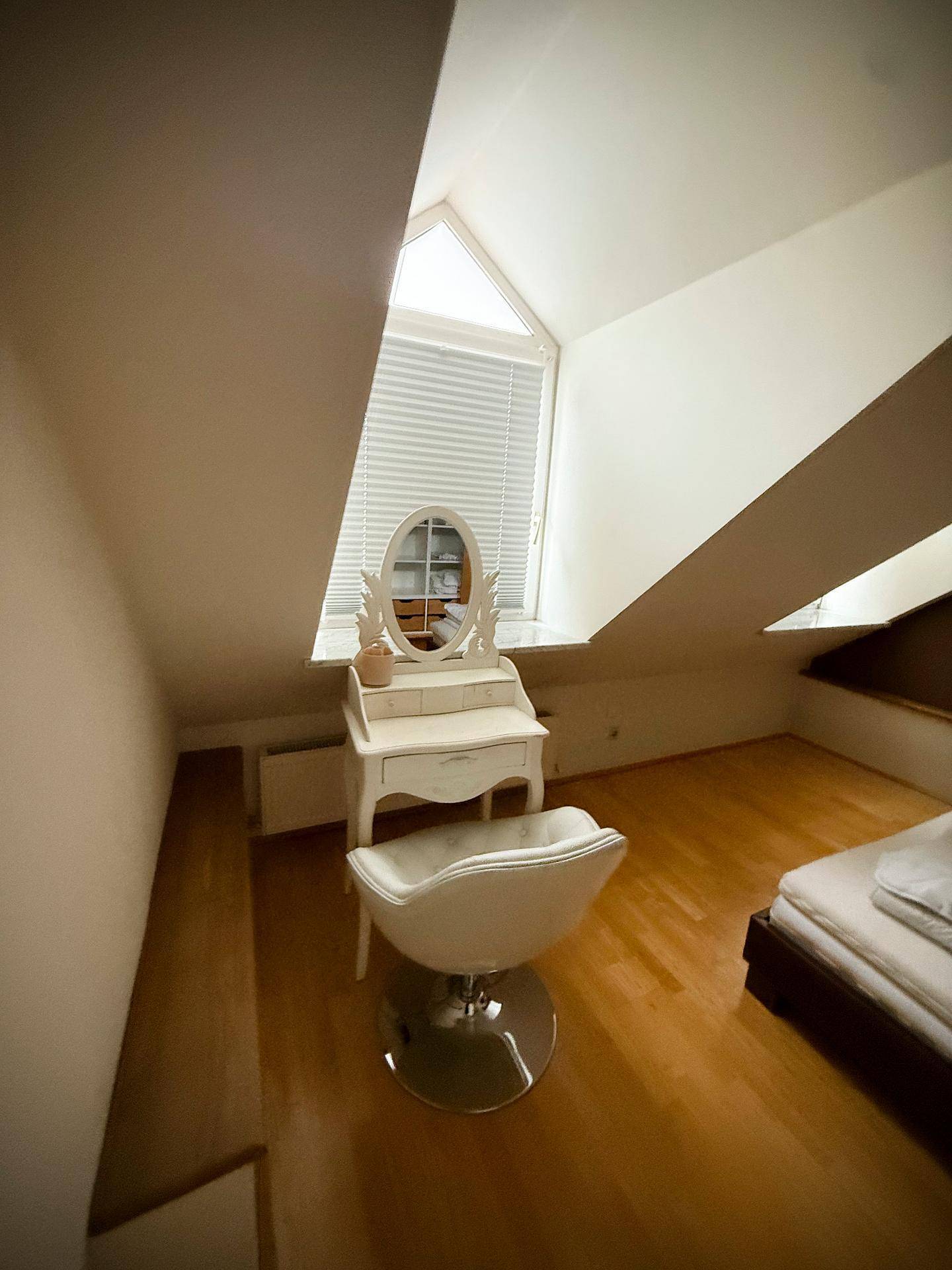Helles Schlafzimmer mit Schminktisch und Fenster in der Dachschräge, das viel Licht spendet.