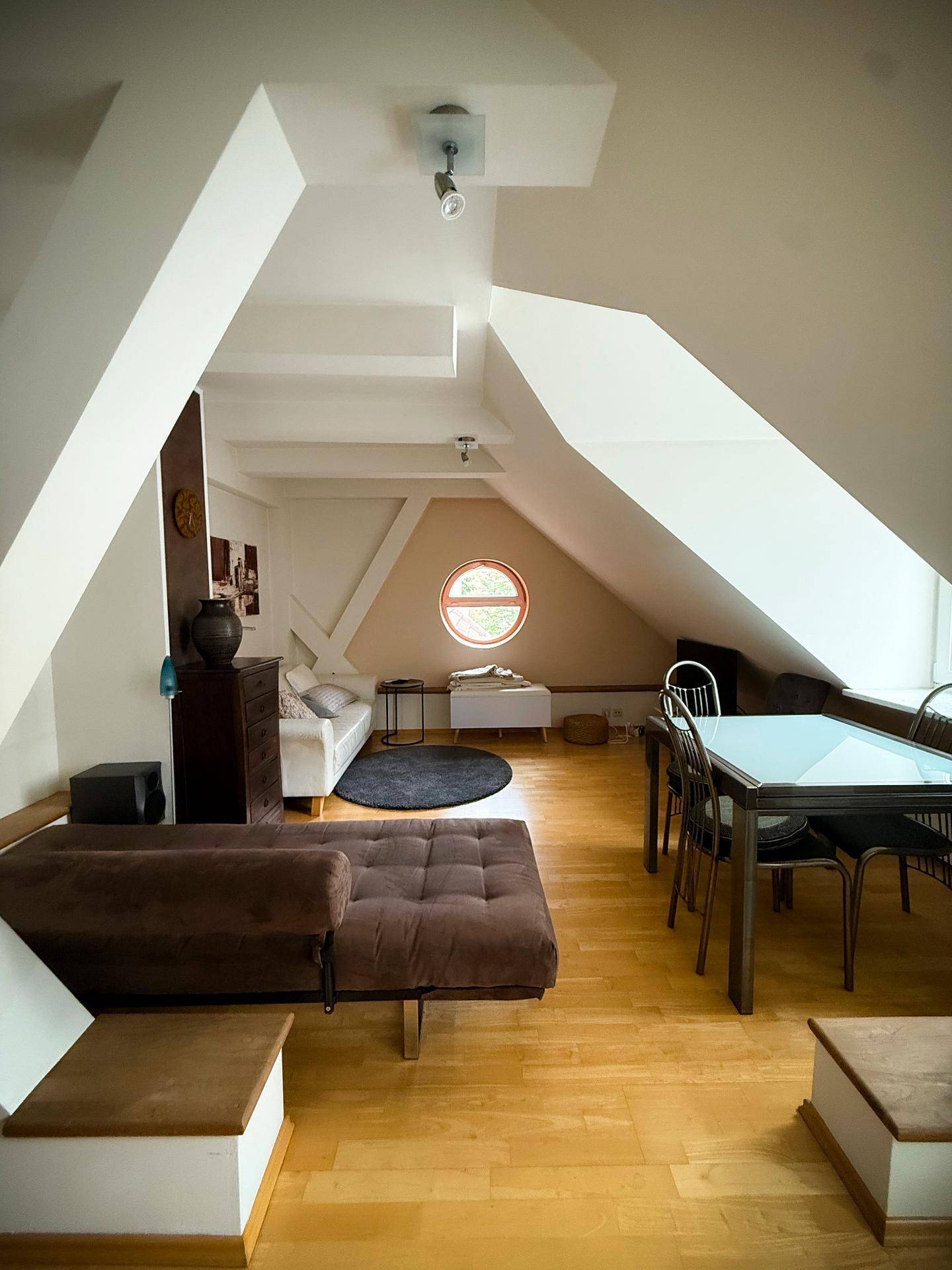 Geräumiger Wohn-Essbereich mit Holzfußboden, Dachschrägen und einem markanten runden Fenster.