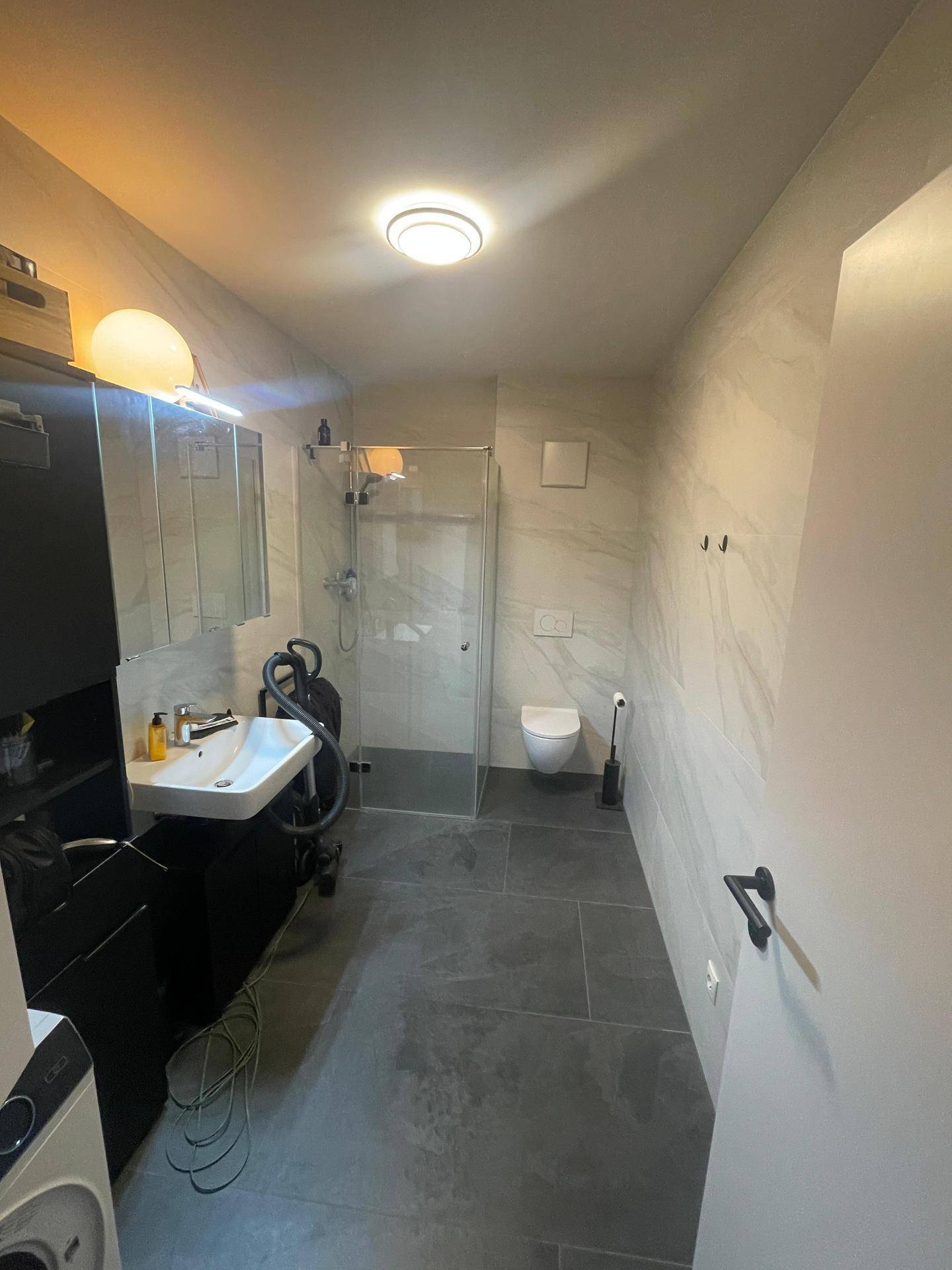 Modernes Badezimmer mit Duschkabine, Einzelwaschbecken und Wand-WC sowie Waschmaschine.