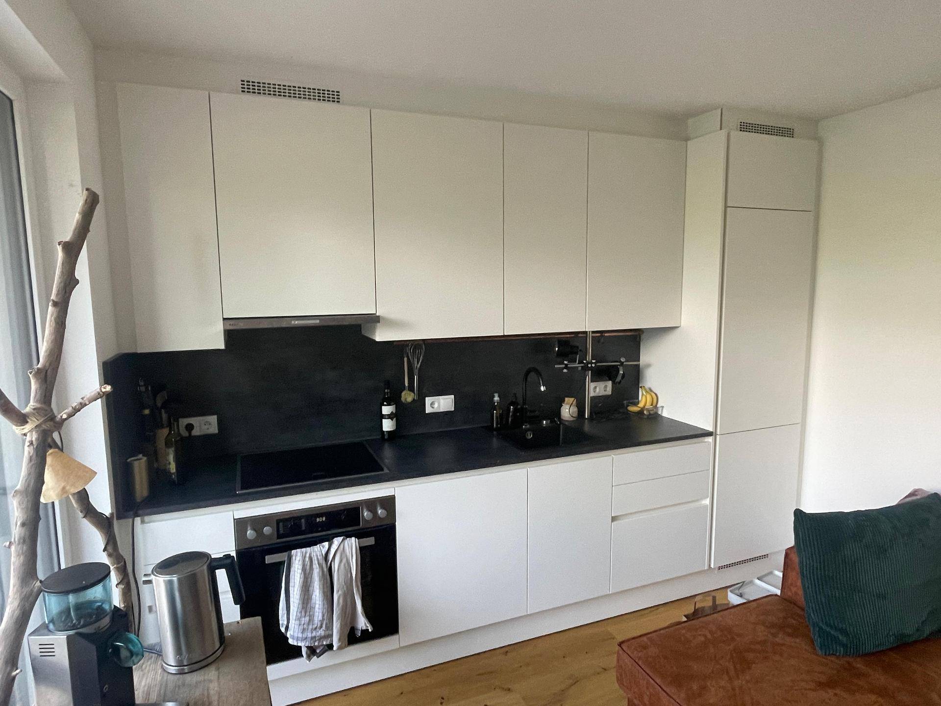 Moderne Einbauküche mit weißen Schränken, schwarzer Arbeitsplatte und integrierten Geräten.