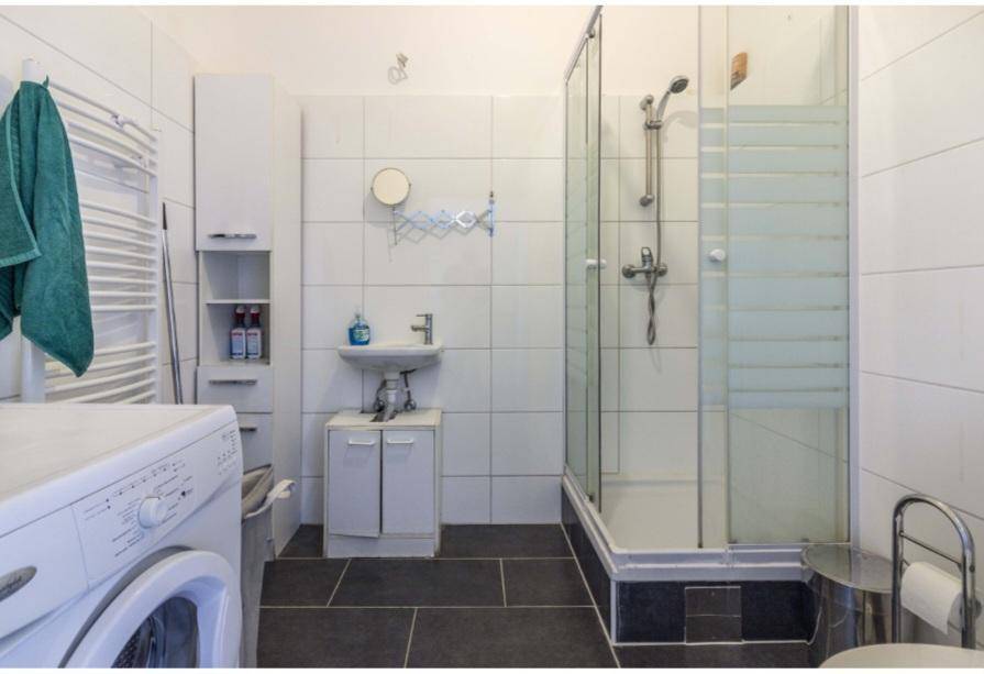 Funktionales Badezimmer mit Duschkabine, Waschbecken, WC und Waschmaschine auf dunklem Fliesenboden.