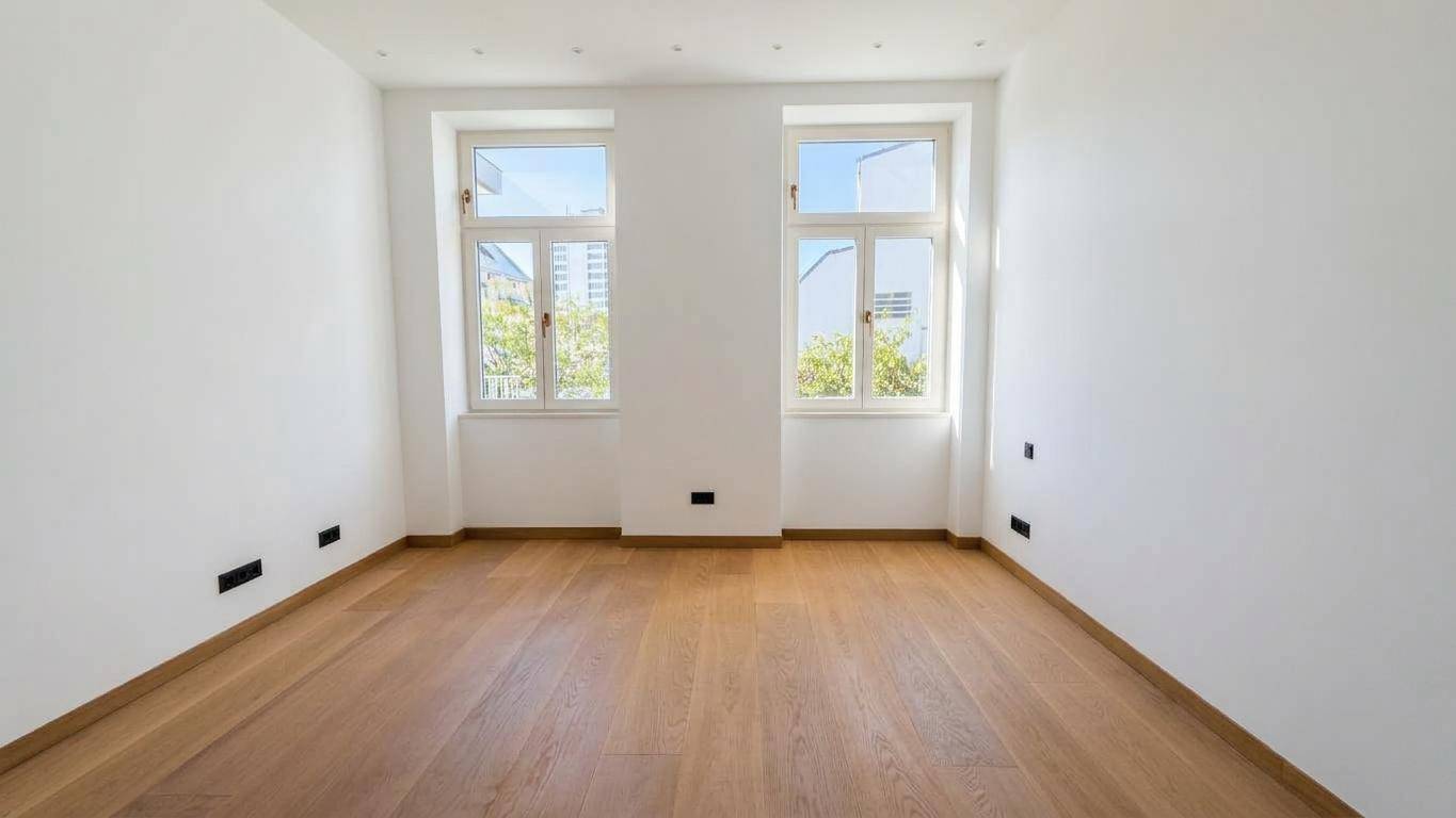 Helles Zimmer mit zwei Fenstern, Parkettboden und weißen Wänden, ideal als Schlaf- oder Arbeitszimmer.
