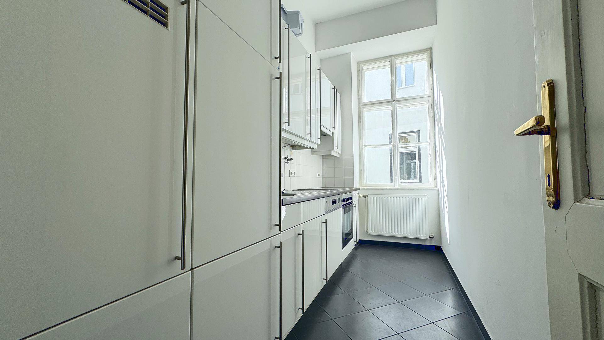 Schmale Küche mit weißen Einbauschränken, dunkler Arbeitsplatte und Fenster für natürliches Licht.