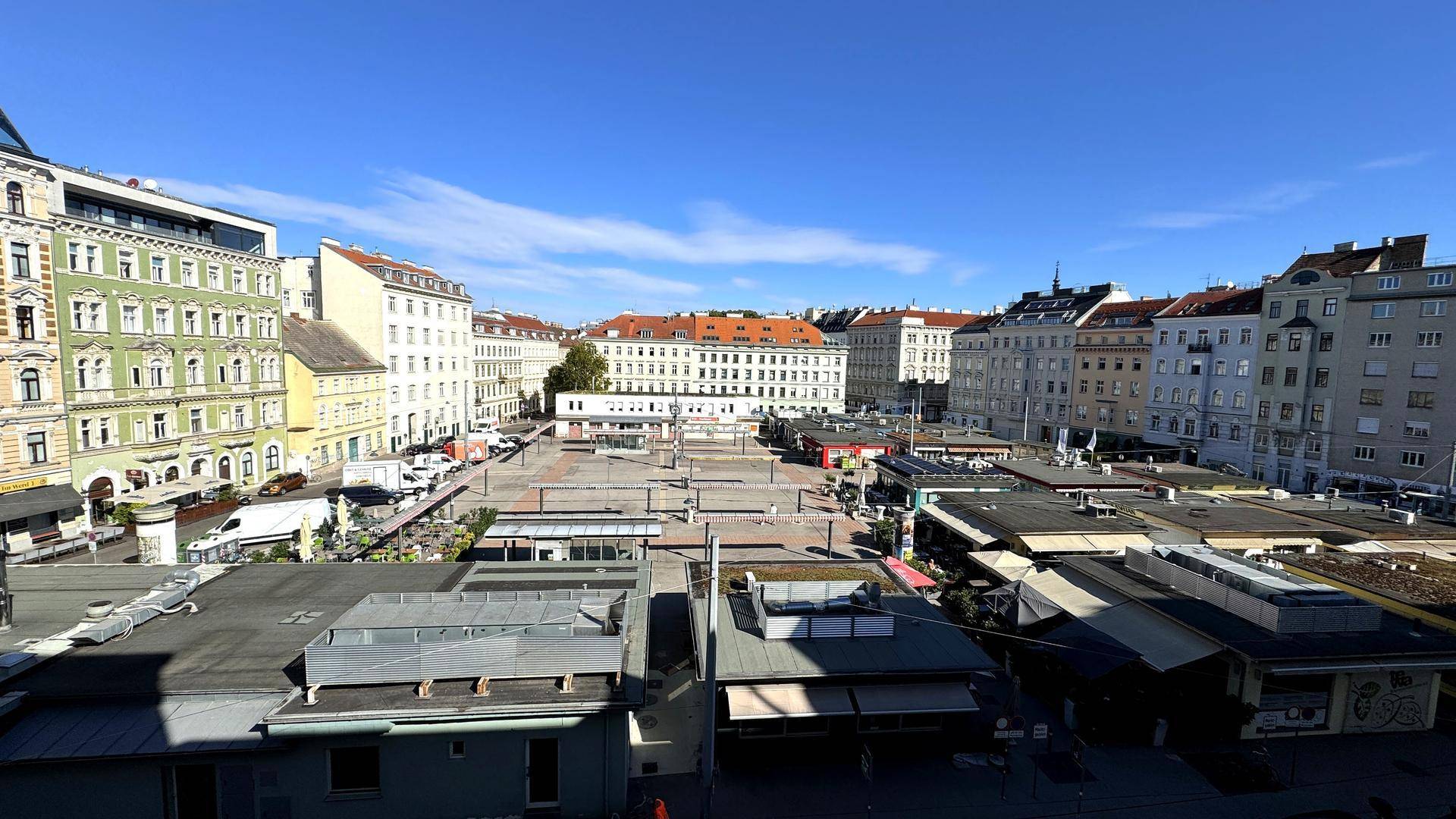 Weitläufiger Blick über einen belebten Stadtplatz mit umliegenden historischen Gebäuden unter blauem Himmel.