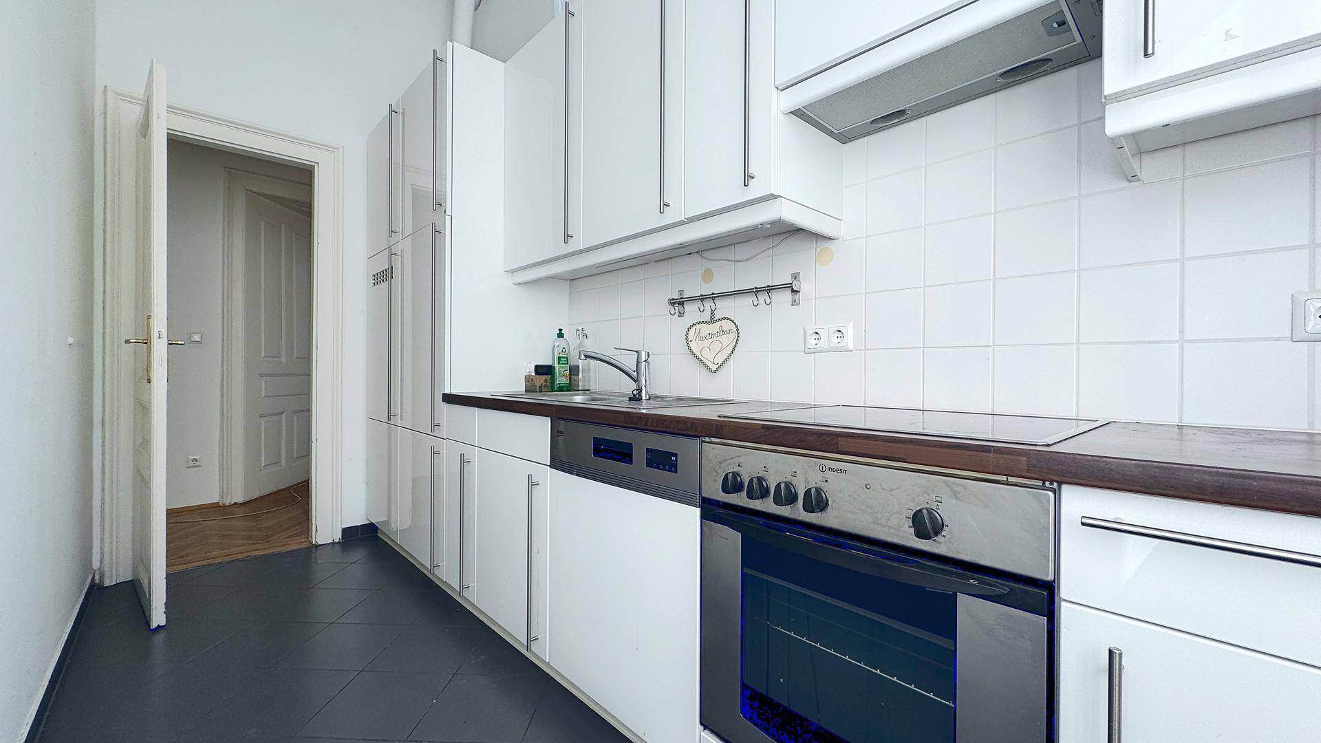 Moderne Küche mit weißen Schränken, Holzarbeitsplatte, Einbauherd, Induktionskochfeld und Spülmaschine.