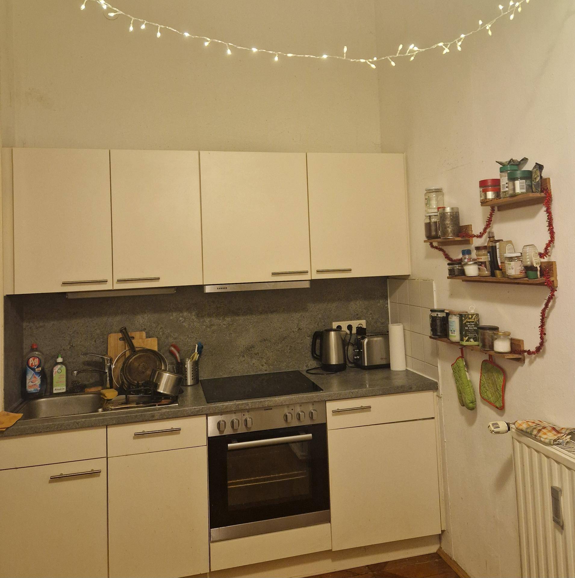Funktionale Küche mit weißen Schränken, integriertem Backofen und Kochfeld, beleuchtet von Lichterketten.