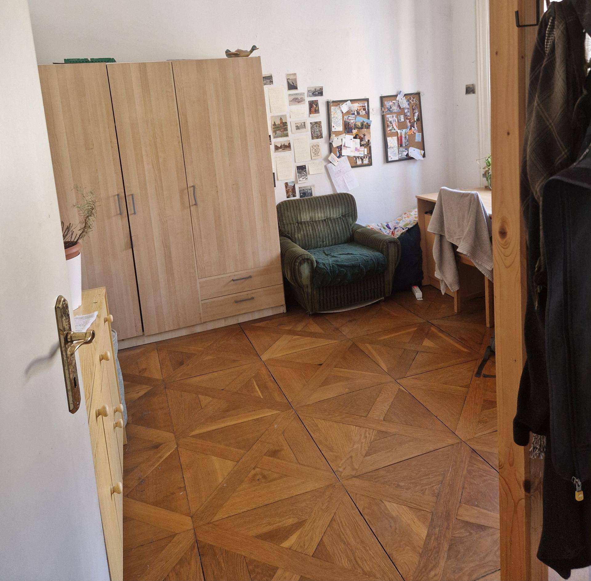 Geräumiges Schlafzimmer mit Parkettboden, Holzschrank, Sessel und Schreibtisch in der Ecke.