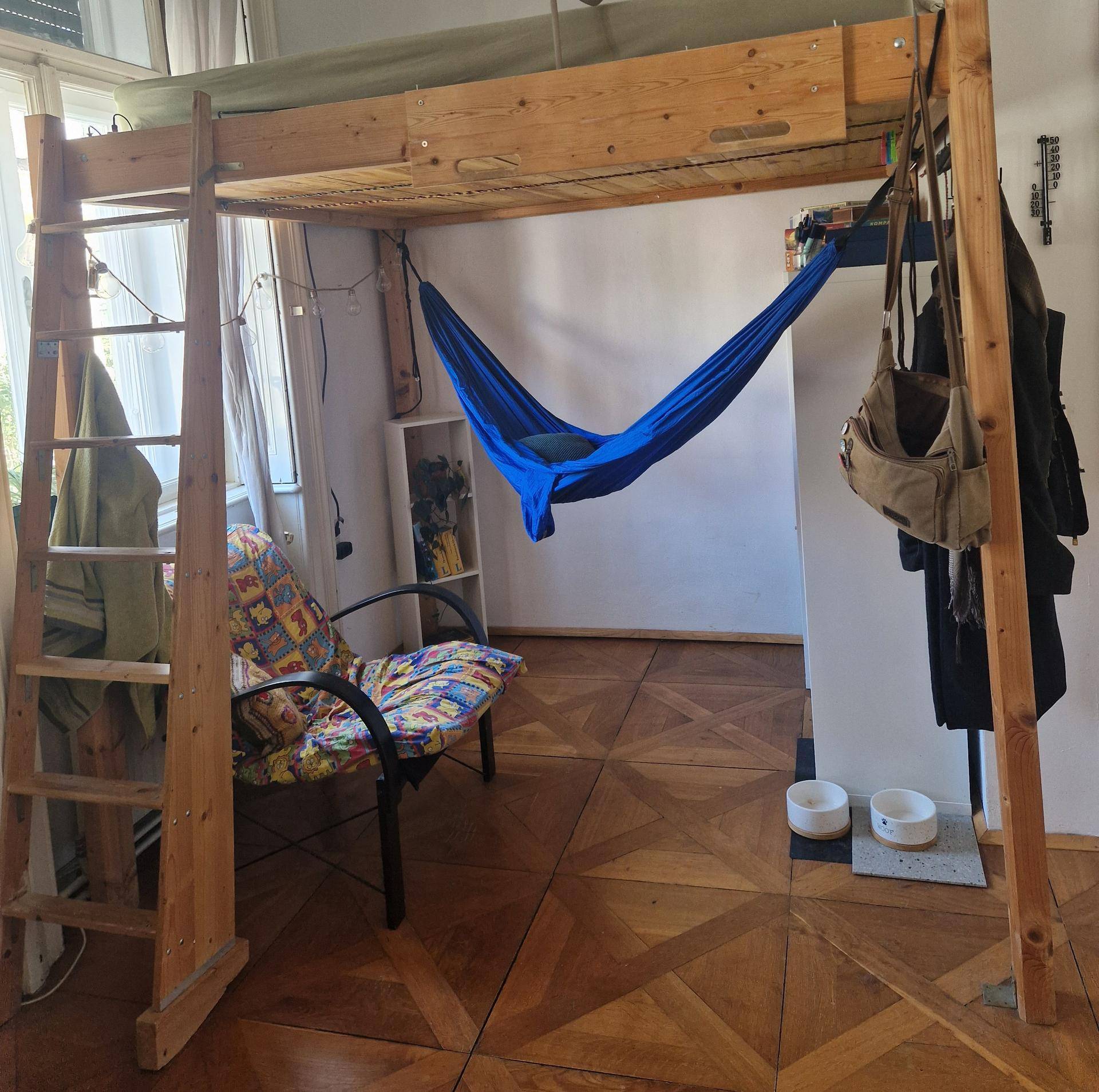 Helles Schlafzimmer mit Hochbett, Hängematte und Fenster mit Vorhängen.