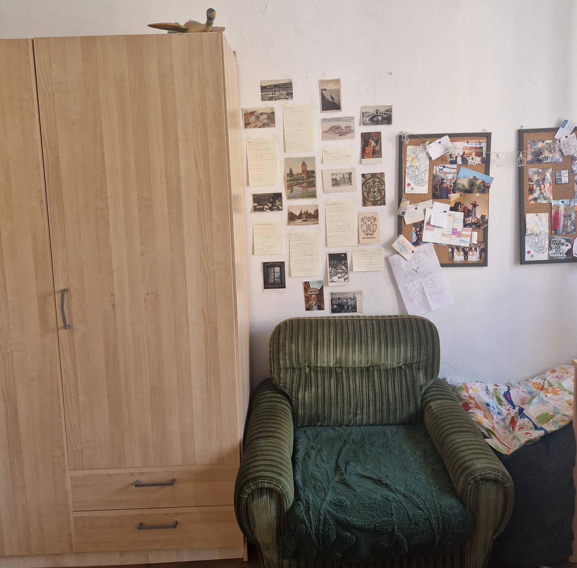 Schlafzimmer mit hellem Holzschrank, grünem Sessel und persönlich gestalteter Wanddekoration.