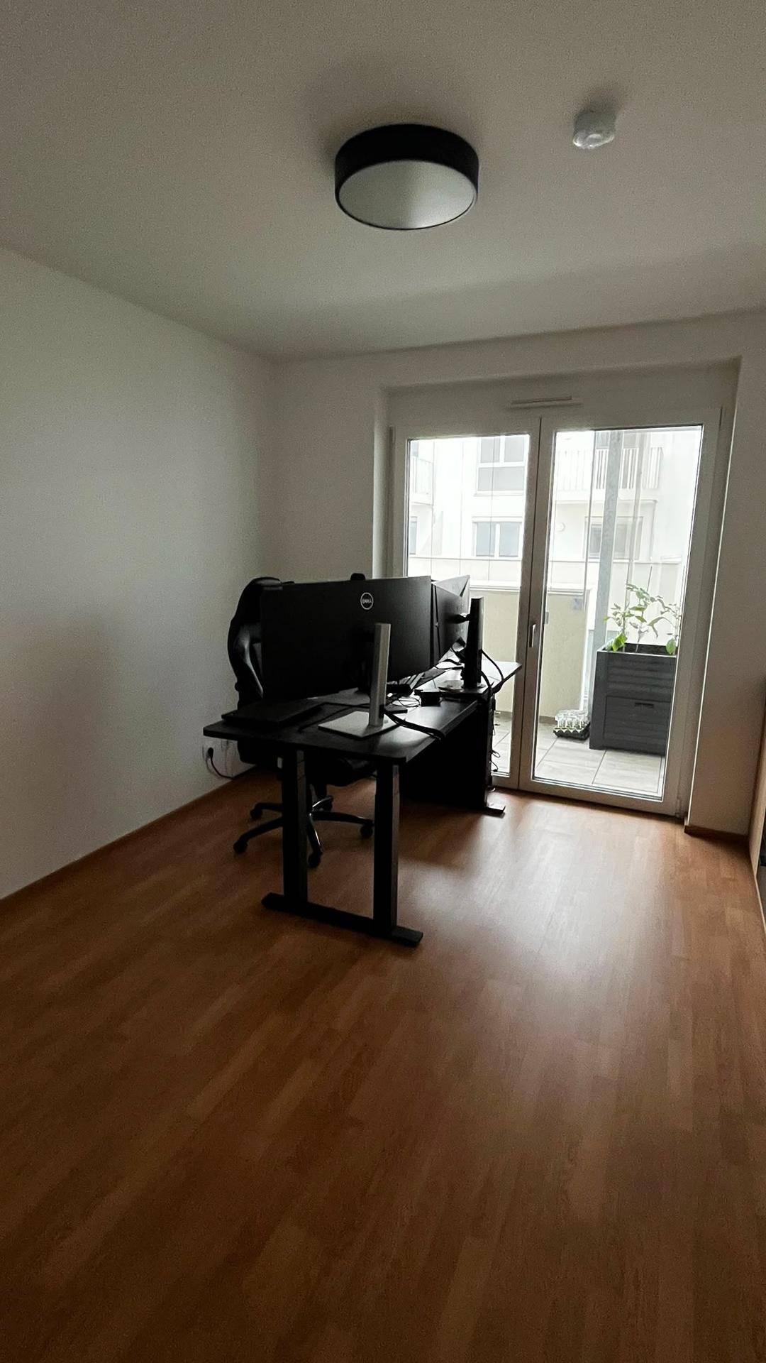 Geräumiges Arbeitszimmer mit Schreibtisch und Monitoren, lichtdurchflutet durch große Balkontür.