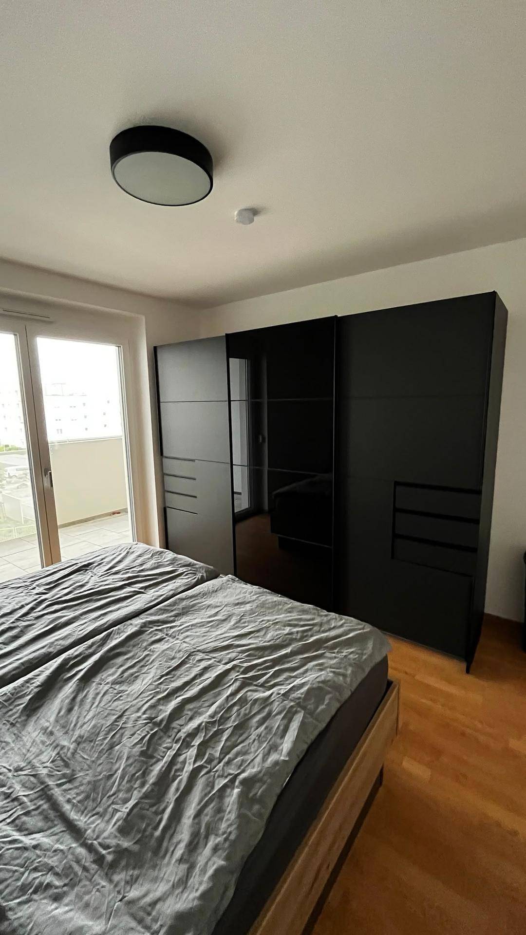 Schlafzimmer mit großem schwarzen Kleiderschrank und Doppelbett, bietet viel Stauraum und Balkonzugang.