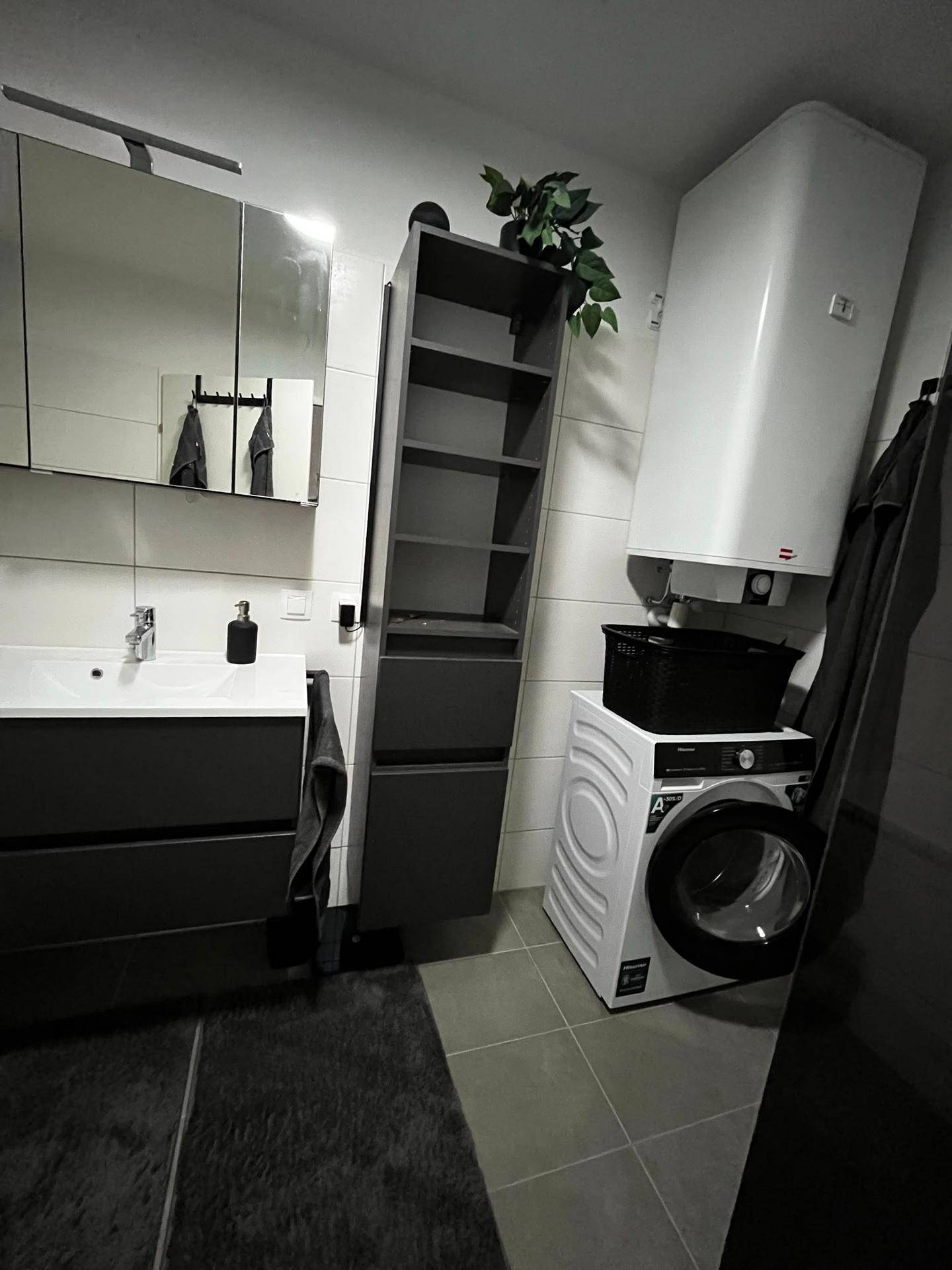Funktionales Badezimmer mit Waschtisch, Spiegelschrank, Waschmaschine und Warmwasserboiler, praktisch eingerichtet.