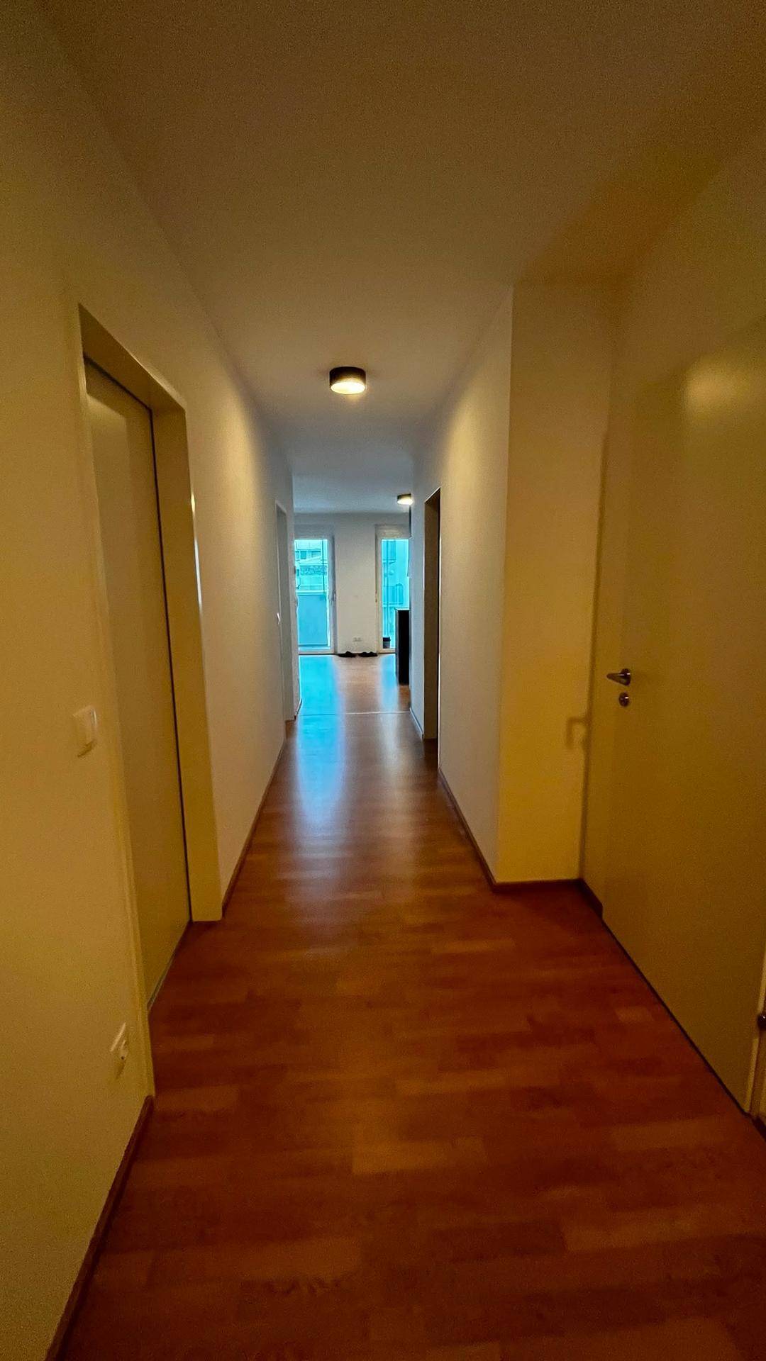 Heller Flur mit Holzboden, der einen Blick in den Wohnbereich und auf den Balkon freigibt.
