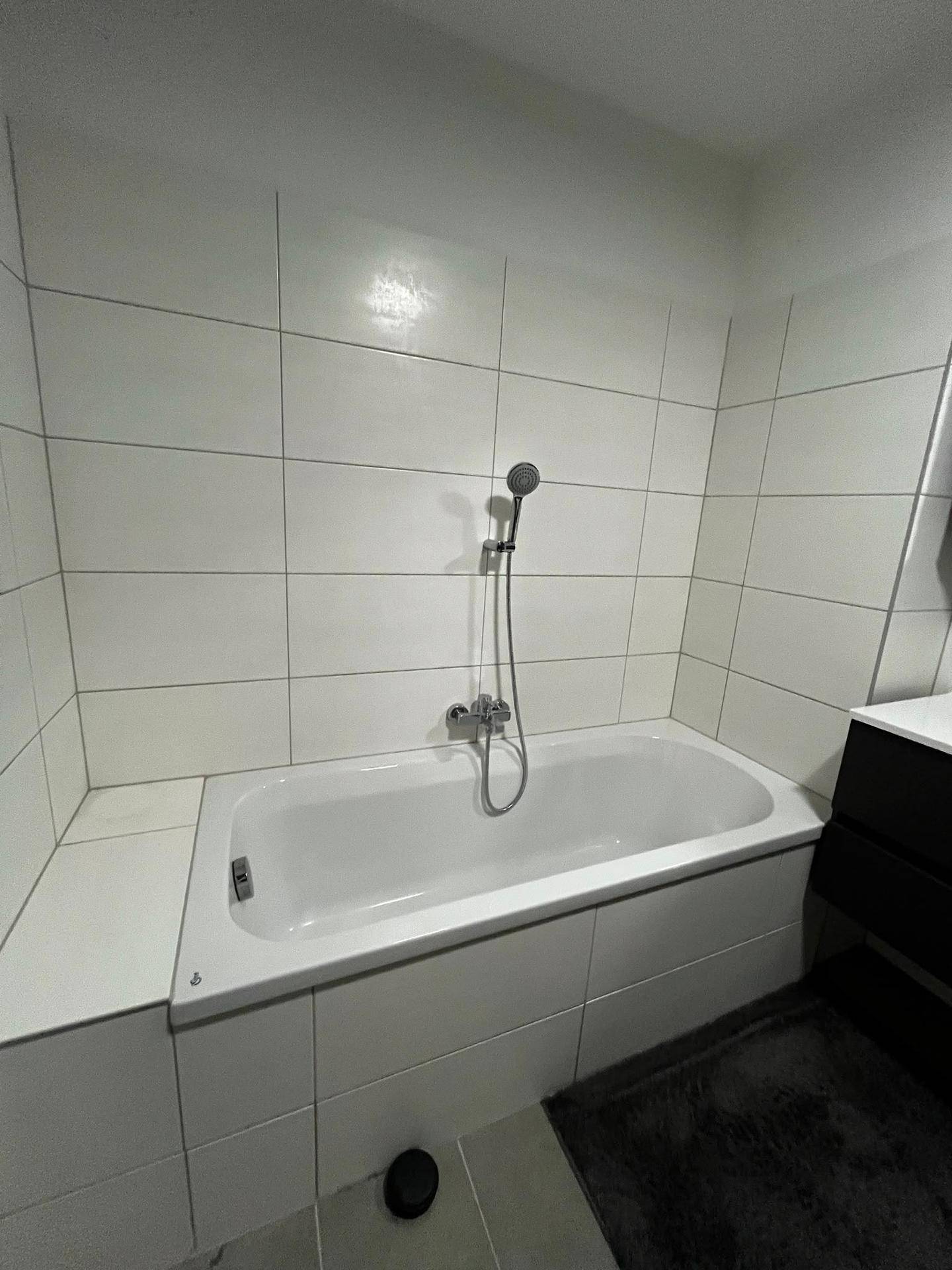 Helles Badezimmer mit weiß gefliester Badewanne und moderner Armatur, sauber und funktional.