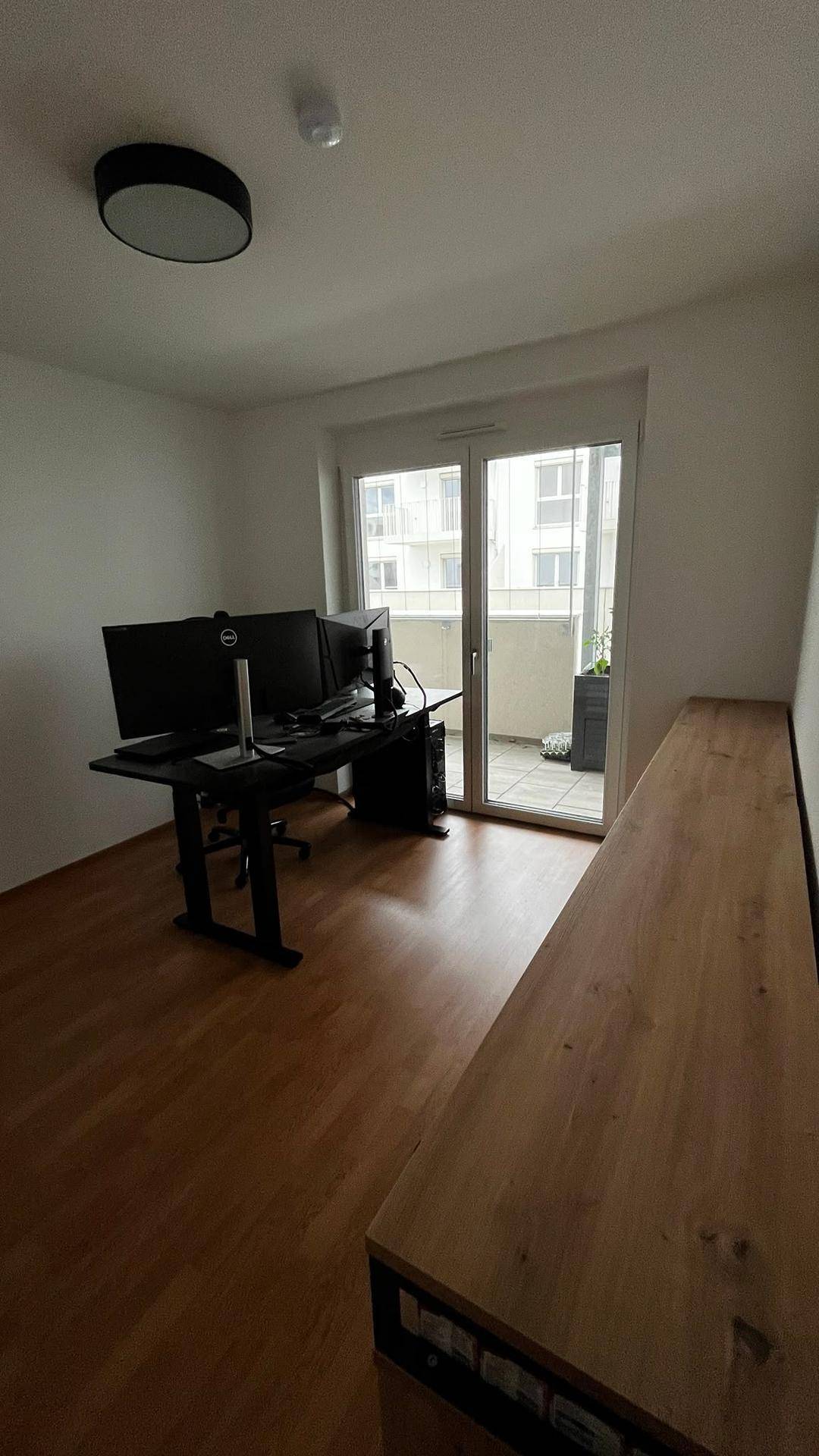 Arbeitszimmer mit Schreibtisch und Monitoren, bietet direkten Zugang zu einem sonnigen Balkon.