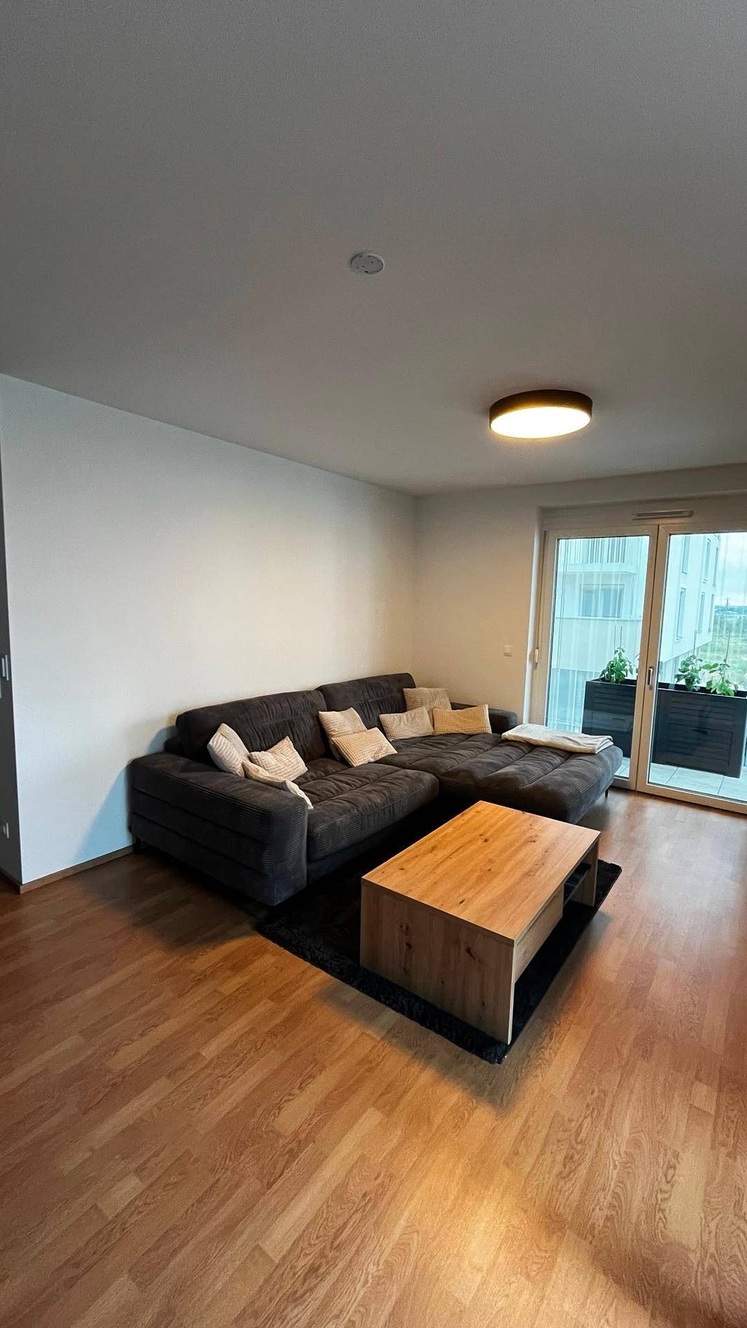 Gemütliches Wohnzimmer mit großem Ecksofa und Holztisch, bietet Zugang zum Balkon.