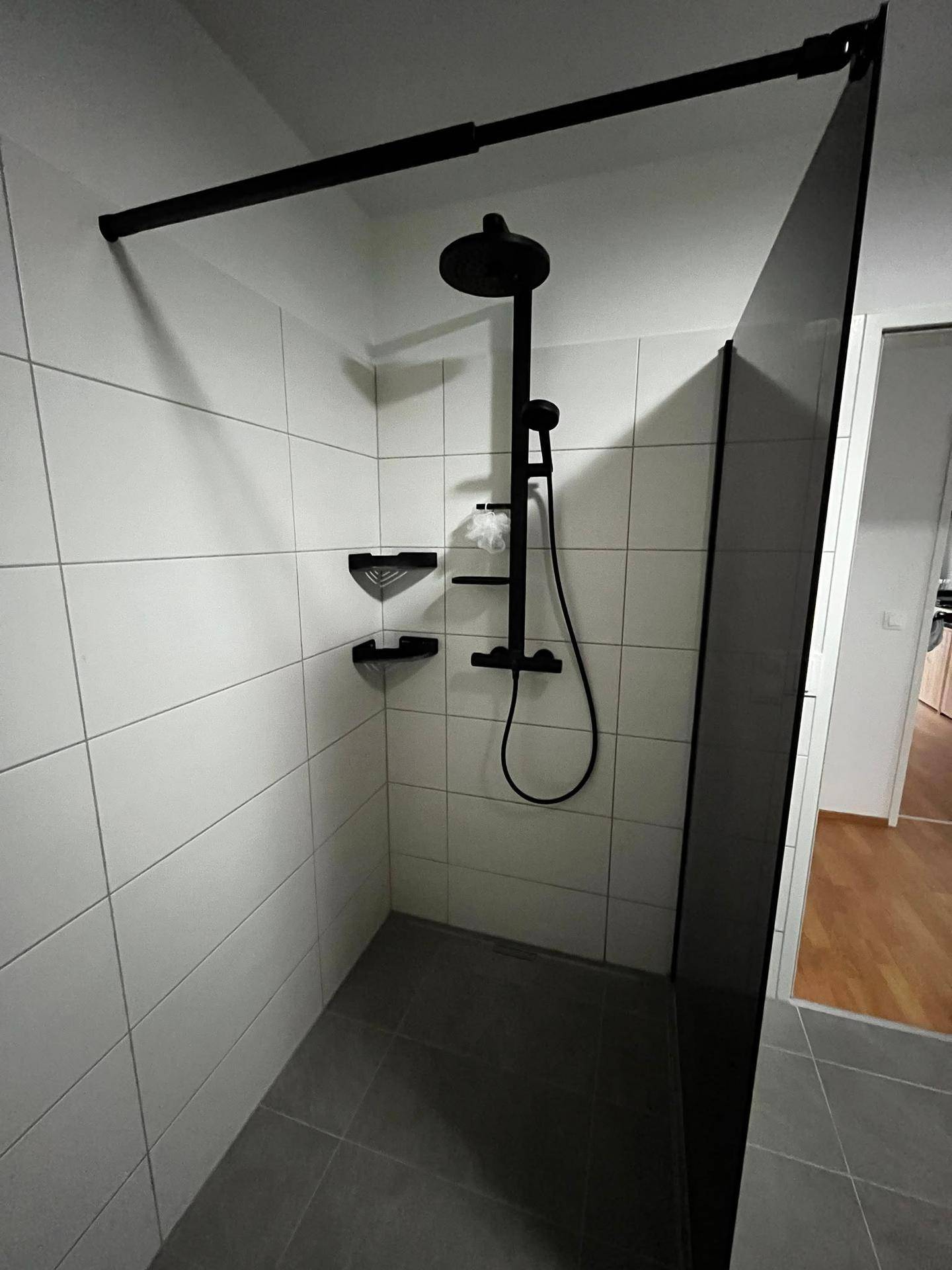 Geräumige begehbare Dusche mit schwarzen Armaturen und weißen Fliesen, modern und leicht zugänglich.