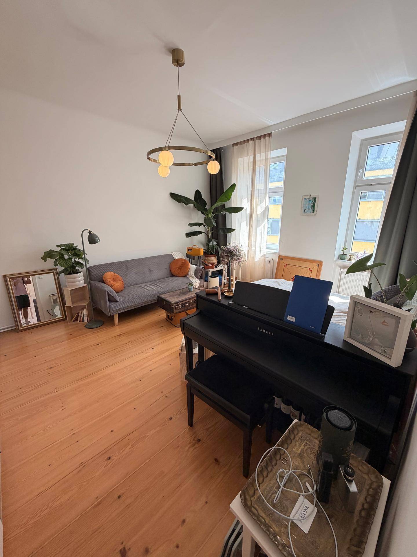 Geräumiges Wohnzimmer mit Holzboden, Sofa, Klavier und viel Tageslicht.