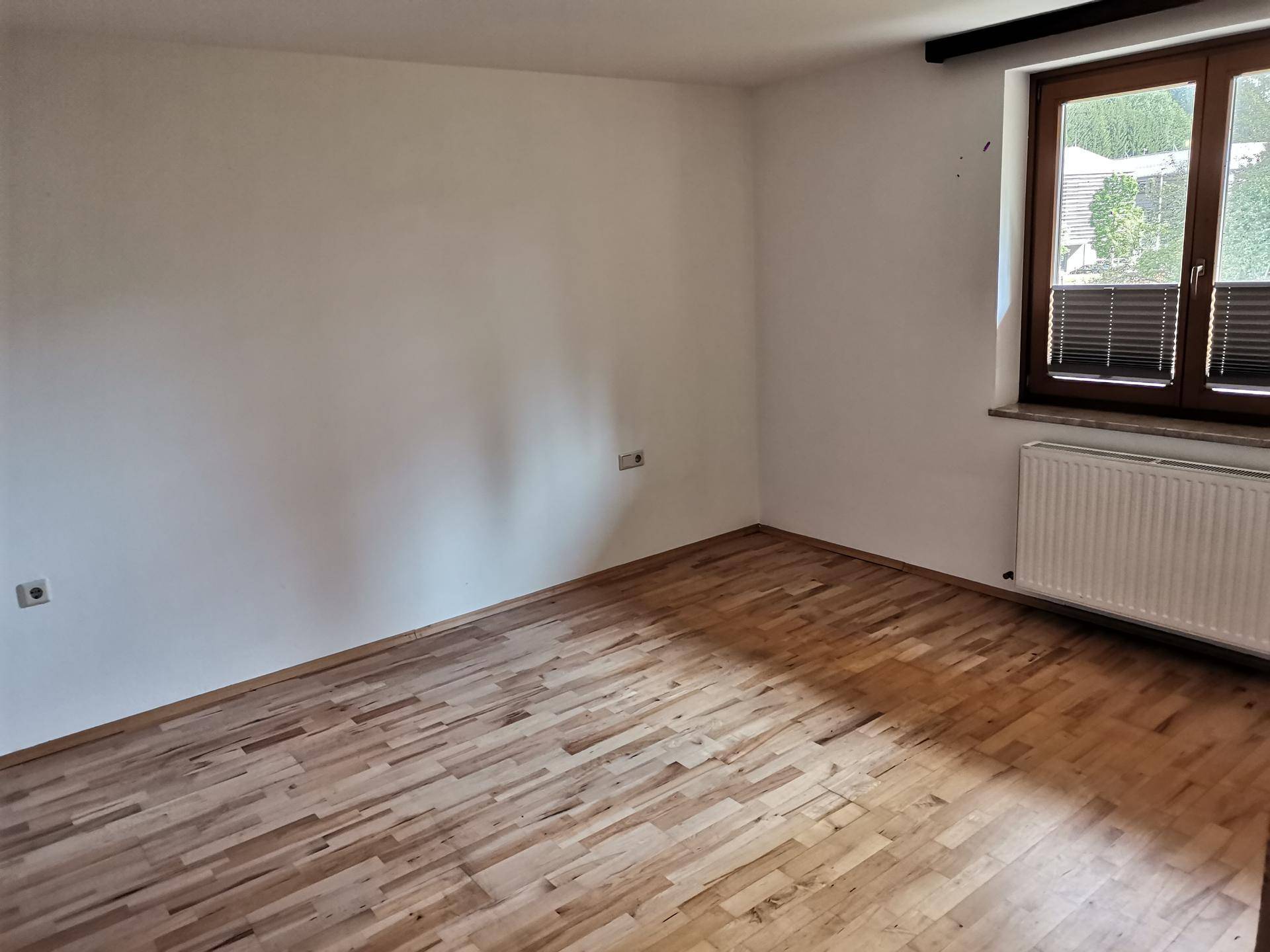Helles Schlafzimmer mit Parkettboden und Fenster mit Jalousien, bereit zur individuellen Gestaltung.