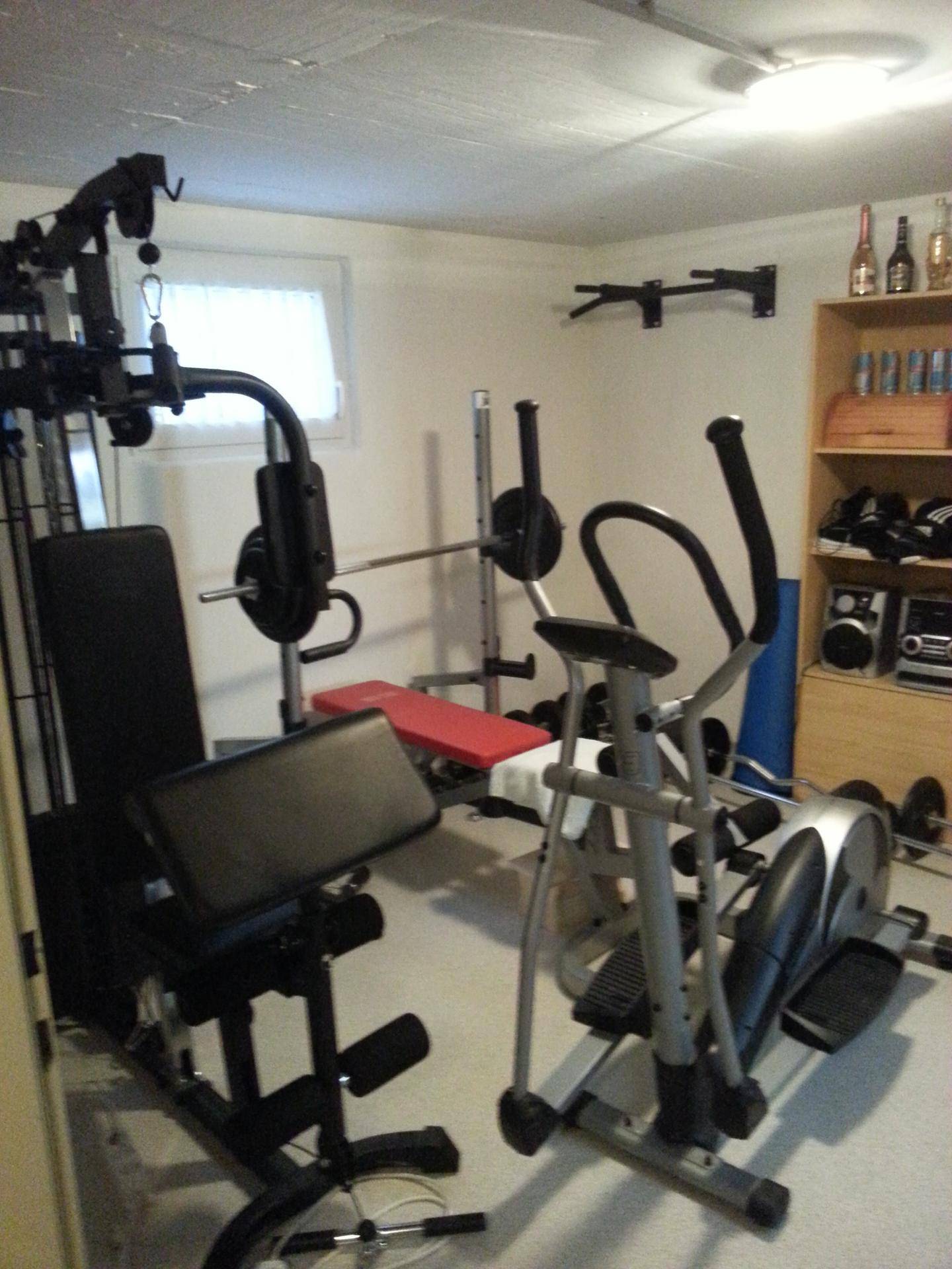 Gut ausgestatteter Fitnessraum im Keller mit verschiedenen Trainingsgeräten für das Heimtraining.