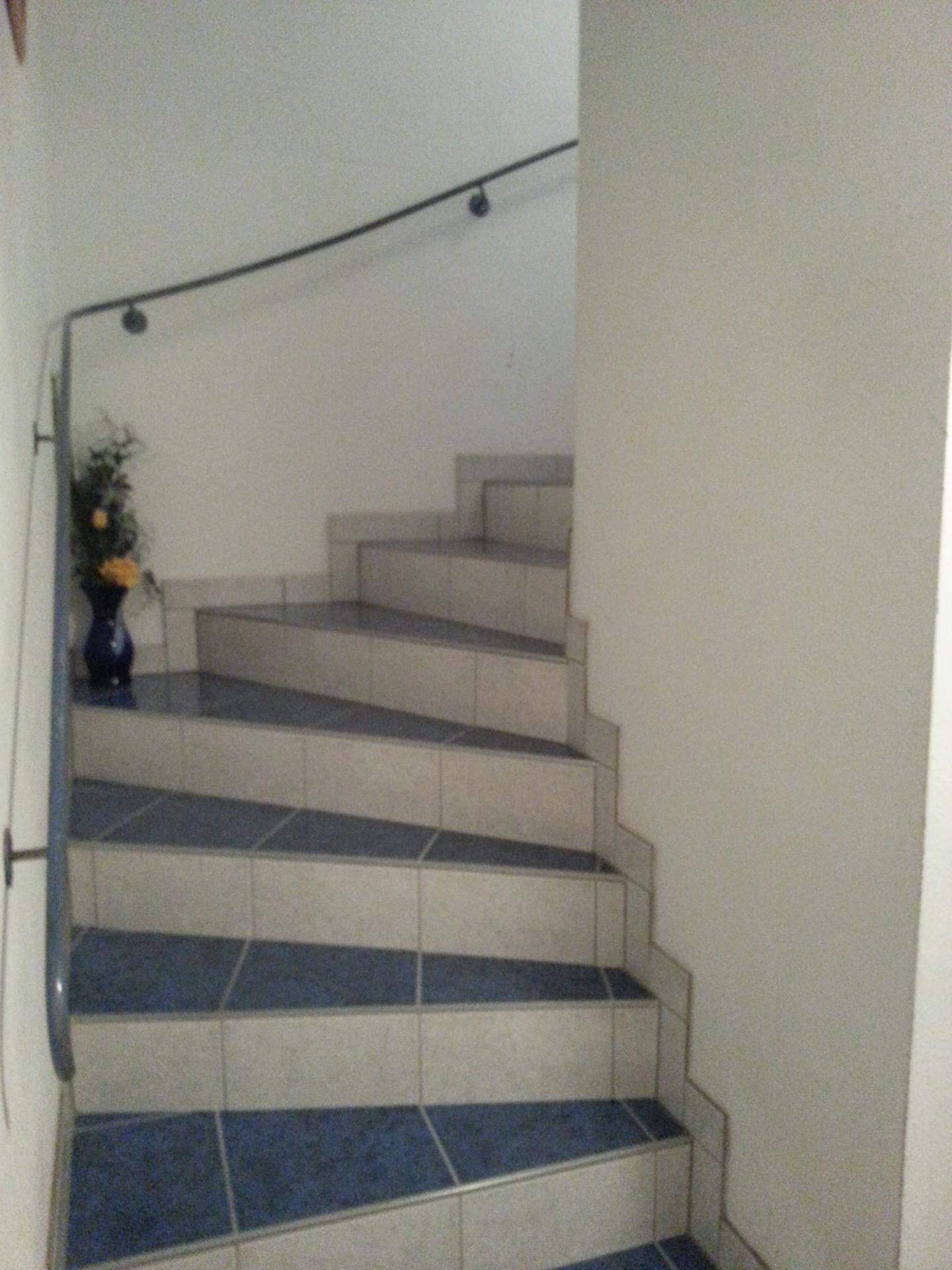 Treppenhaus mit blau-weißen Fliesenstufen und einem schlichten Handlauf.