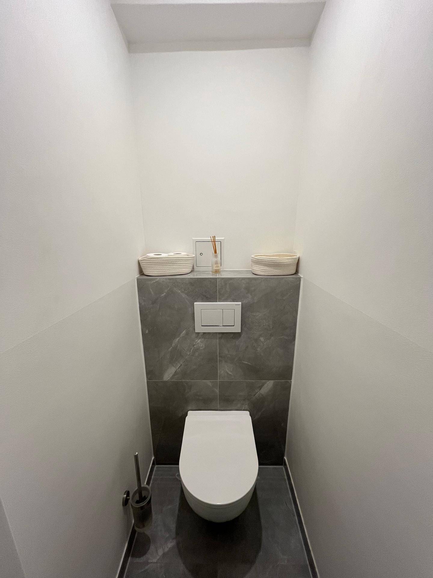 Kleines Gäste-WC mit schlichtem Design und dunklen Fliesenakzenten, sehr gepflegt.