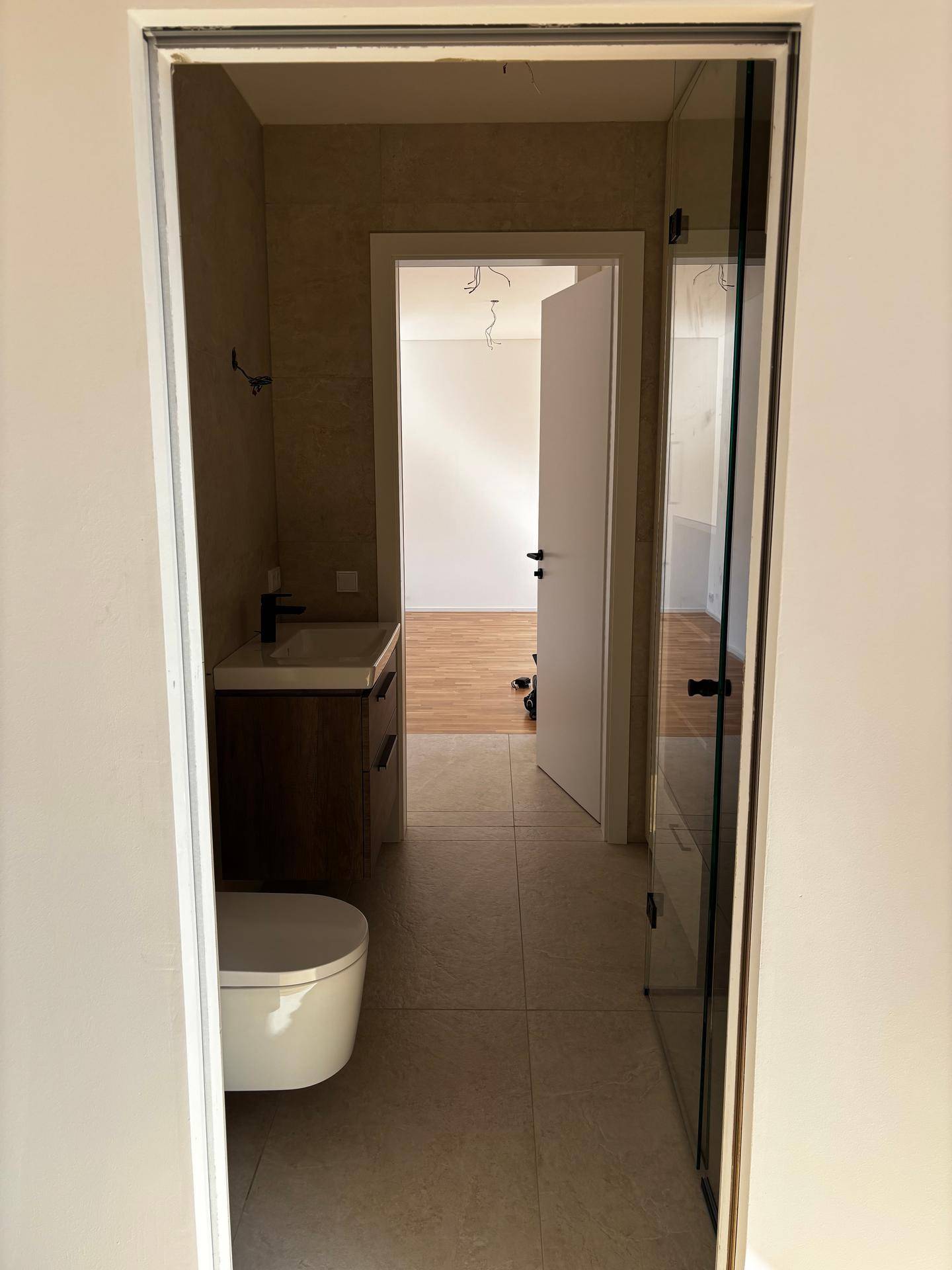 Blick durch die Tür in ein modernes Badezimmer mit WC und Waschtisch, dahinter ein weiterer Raum.